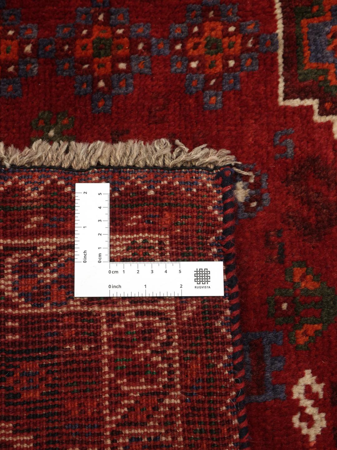 A red hand-knotted wool rug with geometric tribal patterns from the Middle East.