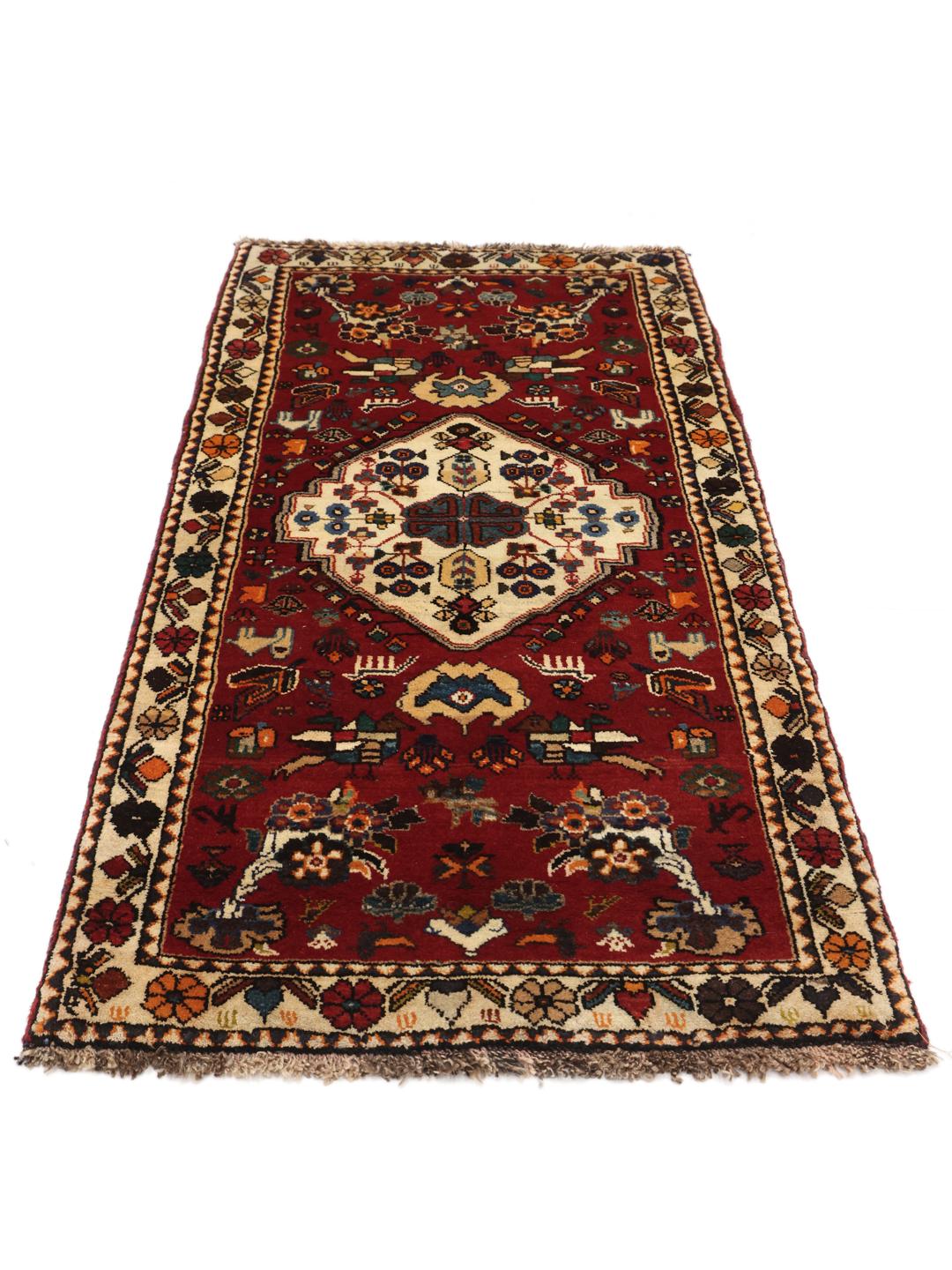 A vibrant red hand-knotted Shiraz rug with intricate geometric tribal patterns and a central medallion.