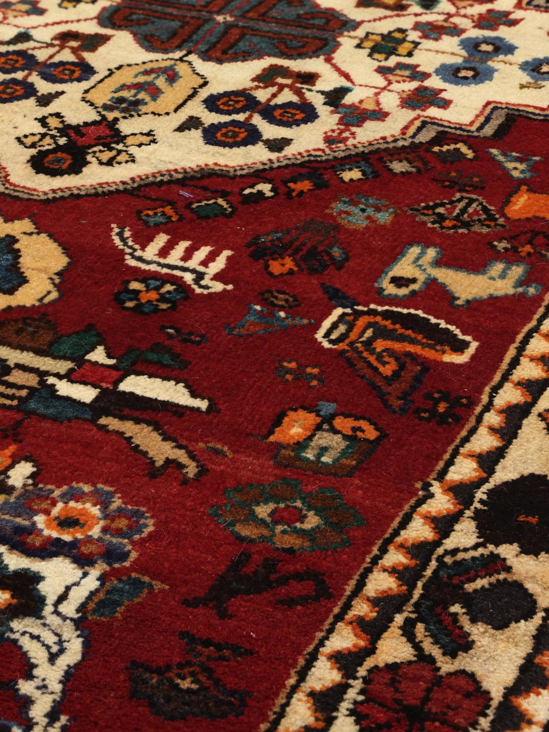 A vibrant red hand-knotted Shiraz rug with intricate geometric tribal patterns and a central medallion.