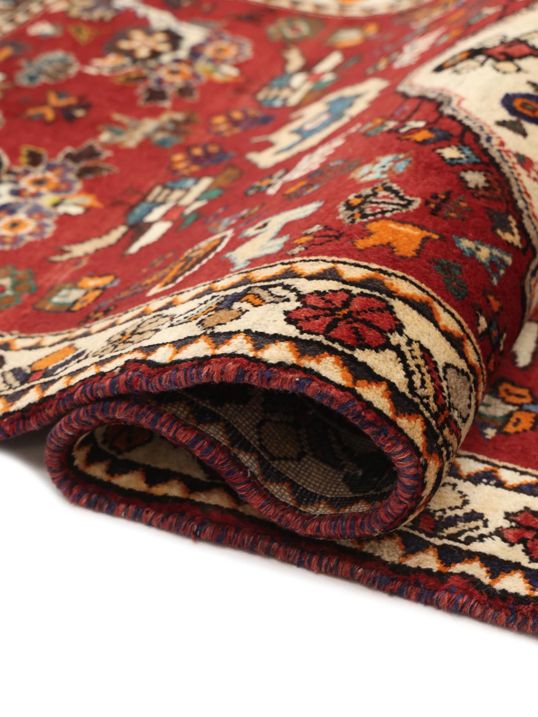 A vibrant red hand-knotted Shiraz rug with intricate geometric tribal patterns and a central medallion.
