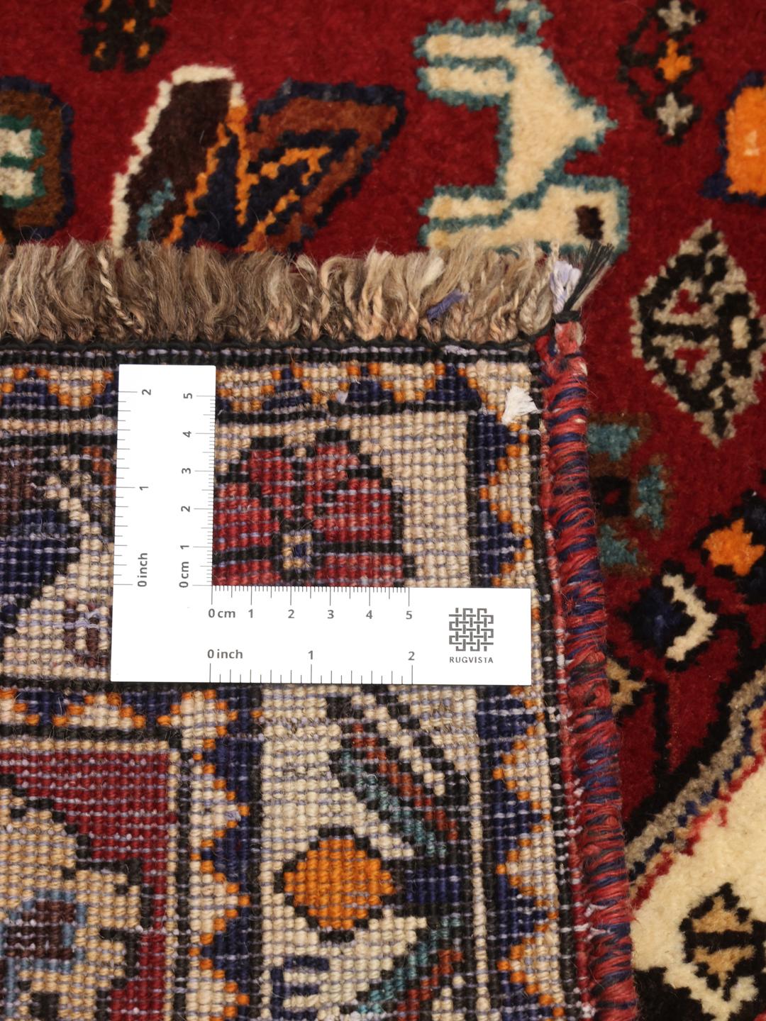 A vibrant red hand-knotted Shiraz rug with intricate geometric tribal patterns and a central medallion.
