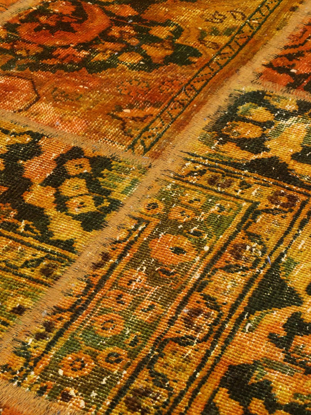 Un tapis patchwork coloré avec des tons orange et vert foncé, présentant des motifs vintage complexes.