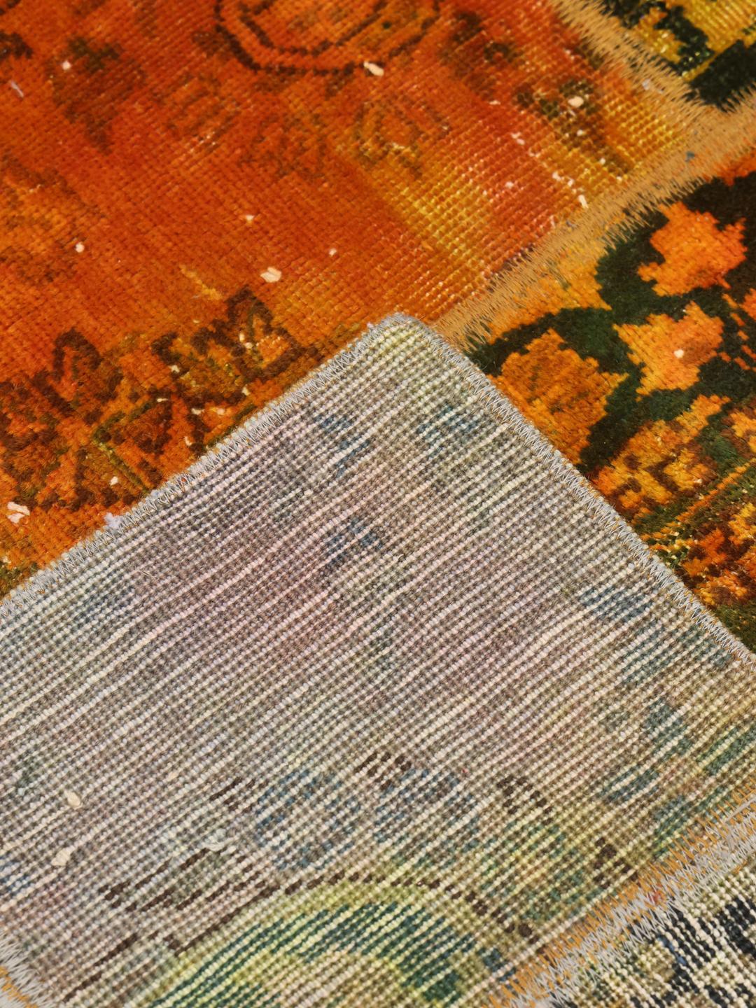 Un tapis patchwork coloré avec des tons orange et vert foncé, présentant des motifs vintage complexes.