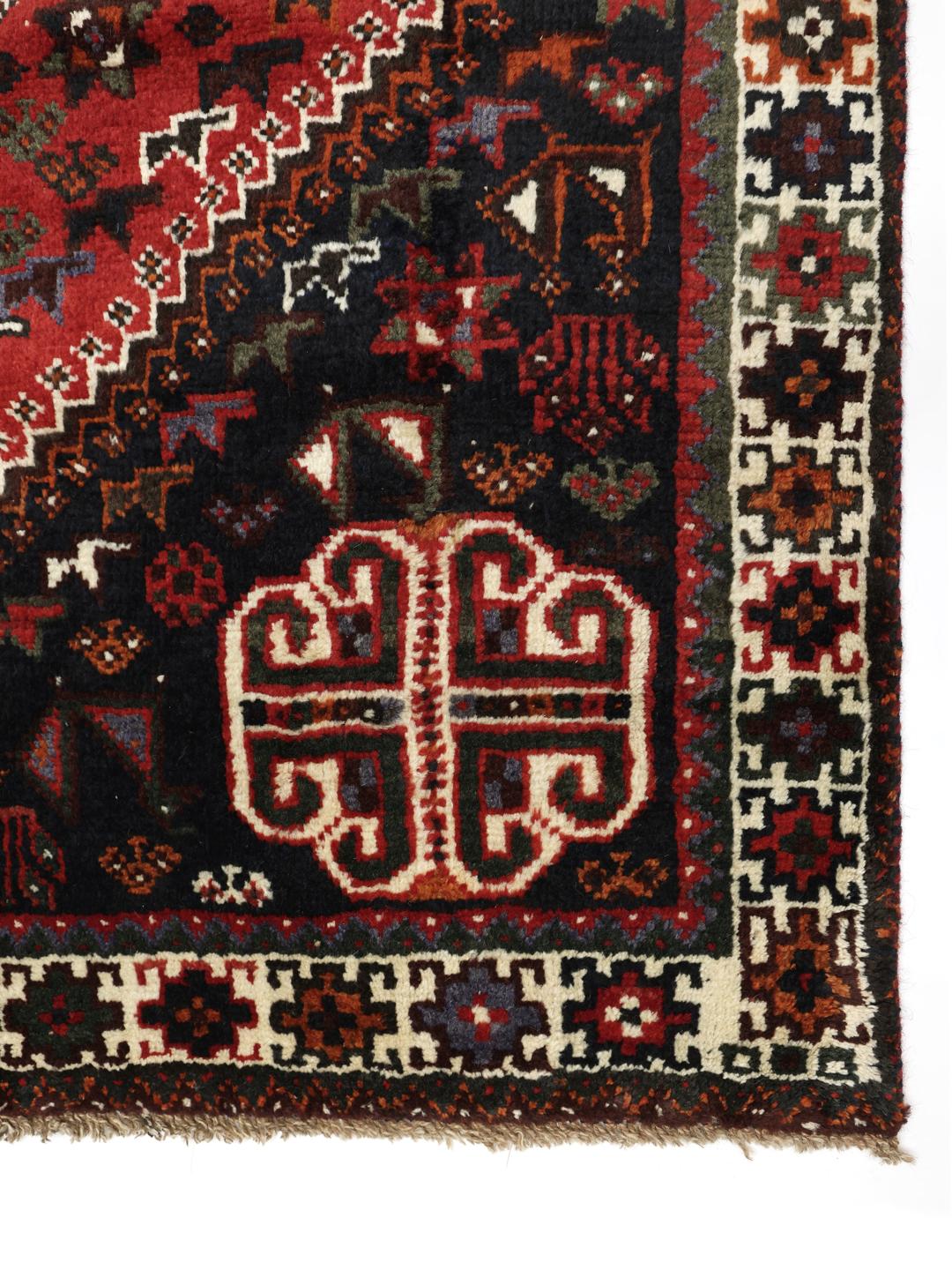 Hand-knotted Qashqai rug with vibrant red and dark tones, originating from the Middle East.