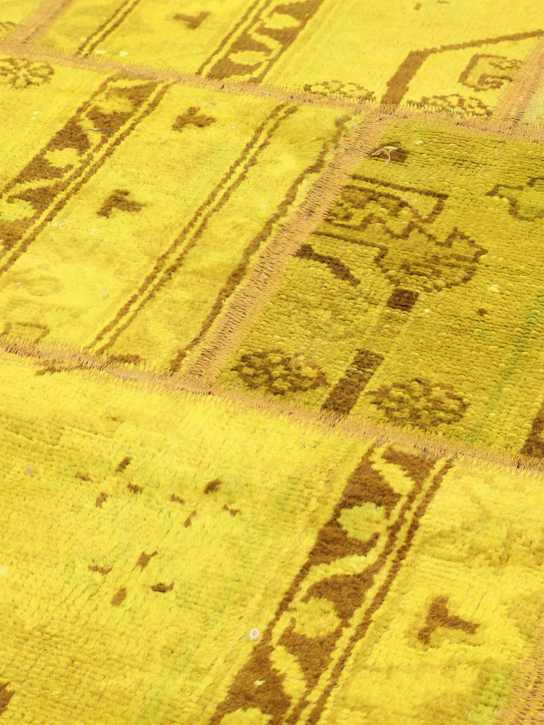 Et levende gult patchwork-tæppe med indviklede mønstre fra Mellemøsten og et unikt håndsyet design.