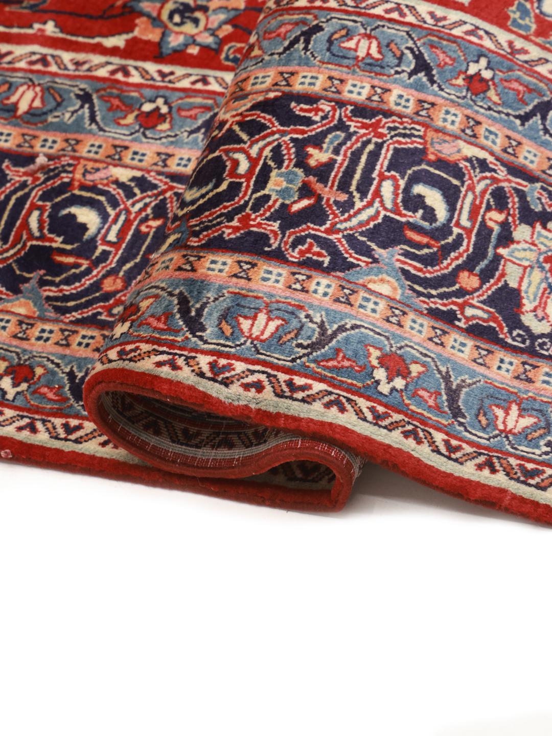 A hand-knotted Sarough rug from the Middle East featuring a vibrant red field with blue floral accents.