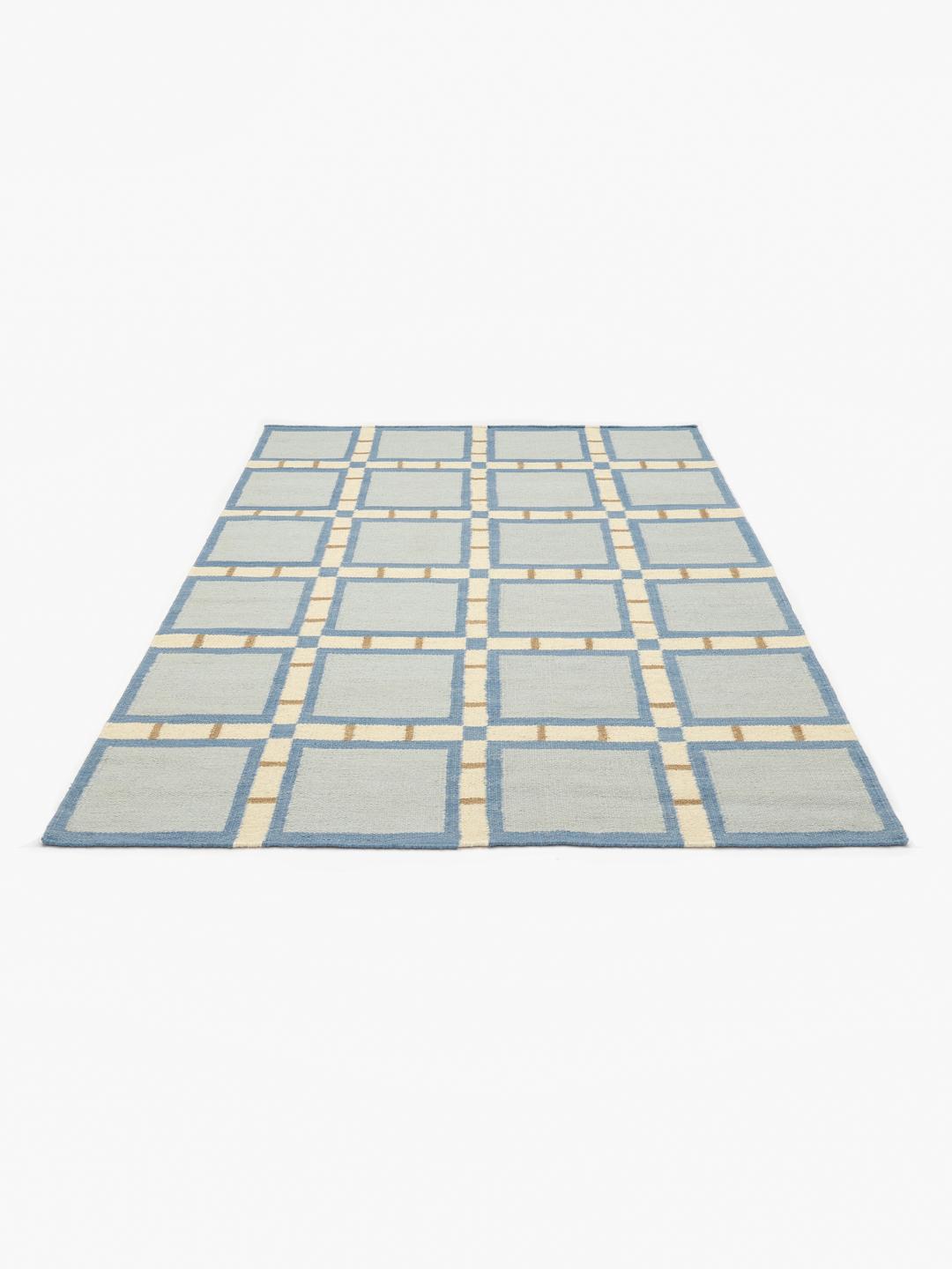 Et rektangulært uldtæppe med et geometrisk gittermønster i blå, beige og hvide nuancer.