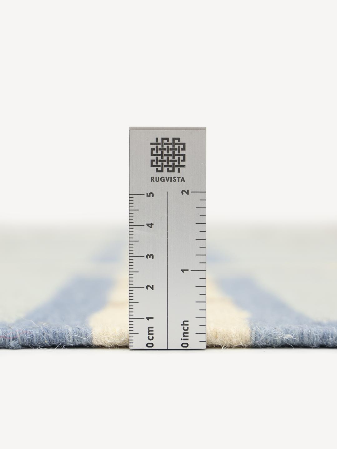 Et rektangulært uldtæppe med et geometrisk gittermønster i blå, beige og hvide nuancer.