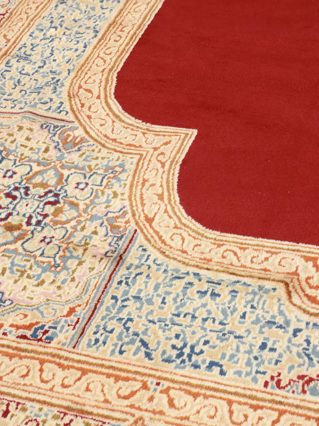 Een groot rechthoekig Kerman-tapijt uit het Midden-Oosten met een rood veld en een ingewikkeld blauw en beige medaillon.