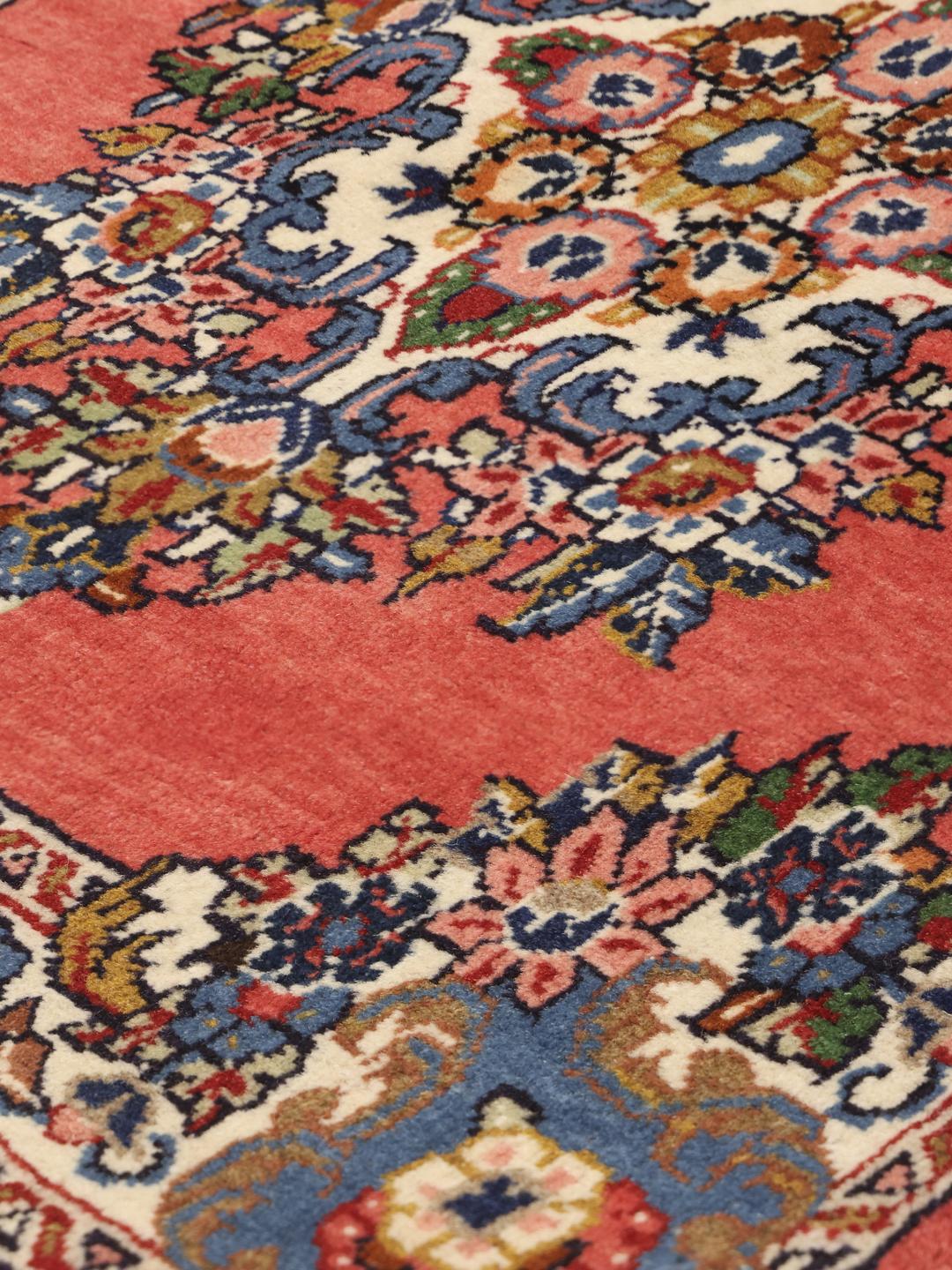 A hand-knotted Sarough rug from the Middle East featuring a vibrant red field and a detailed floral medallion.