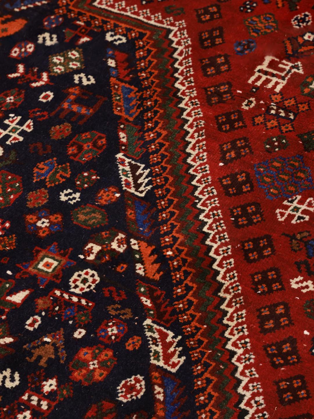 A hand-knotted Qashqai rug from the Middle East featuring a vibrant red and navy blue geometric tribal pattern.