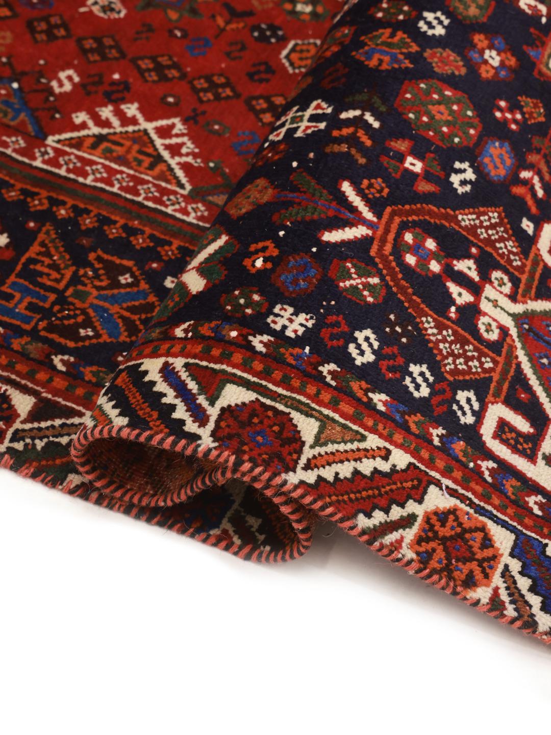 A hand-knotted Qashqai rug from the Middle East featuring a vibrant red and navy blue geometric tribal pattern.