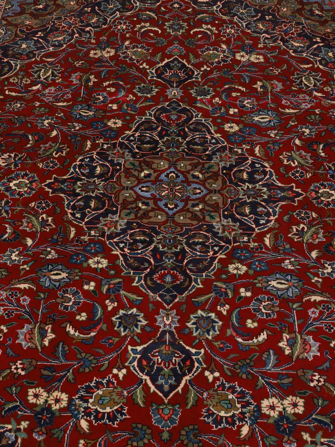 A hand-knotted Mashad rug from the Middle East with a deep red field and ornate patterns.