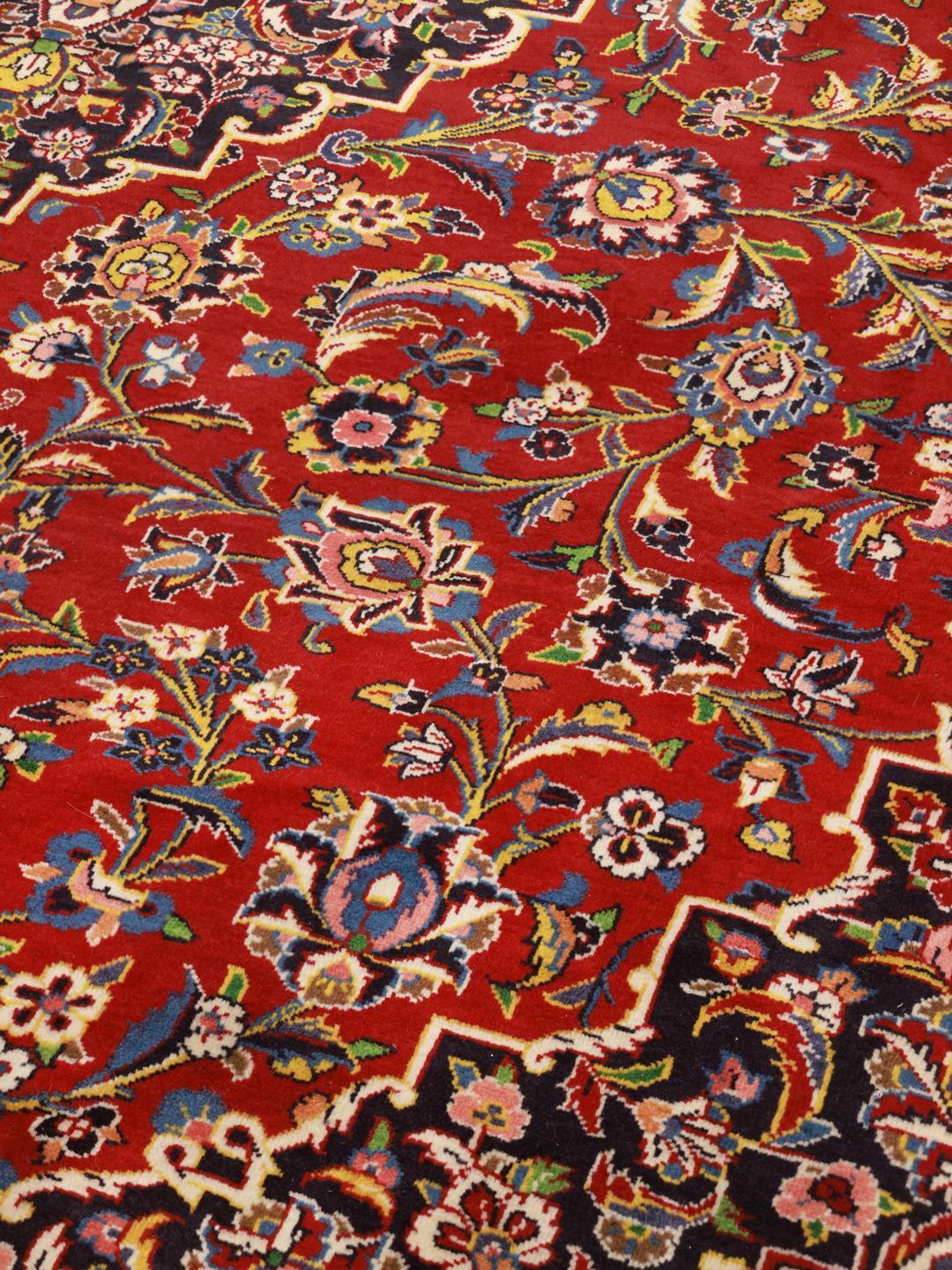 A large, hand-knotted Keshan rug from the Middle East with a deep red floral field and navy border.