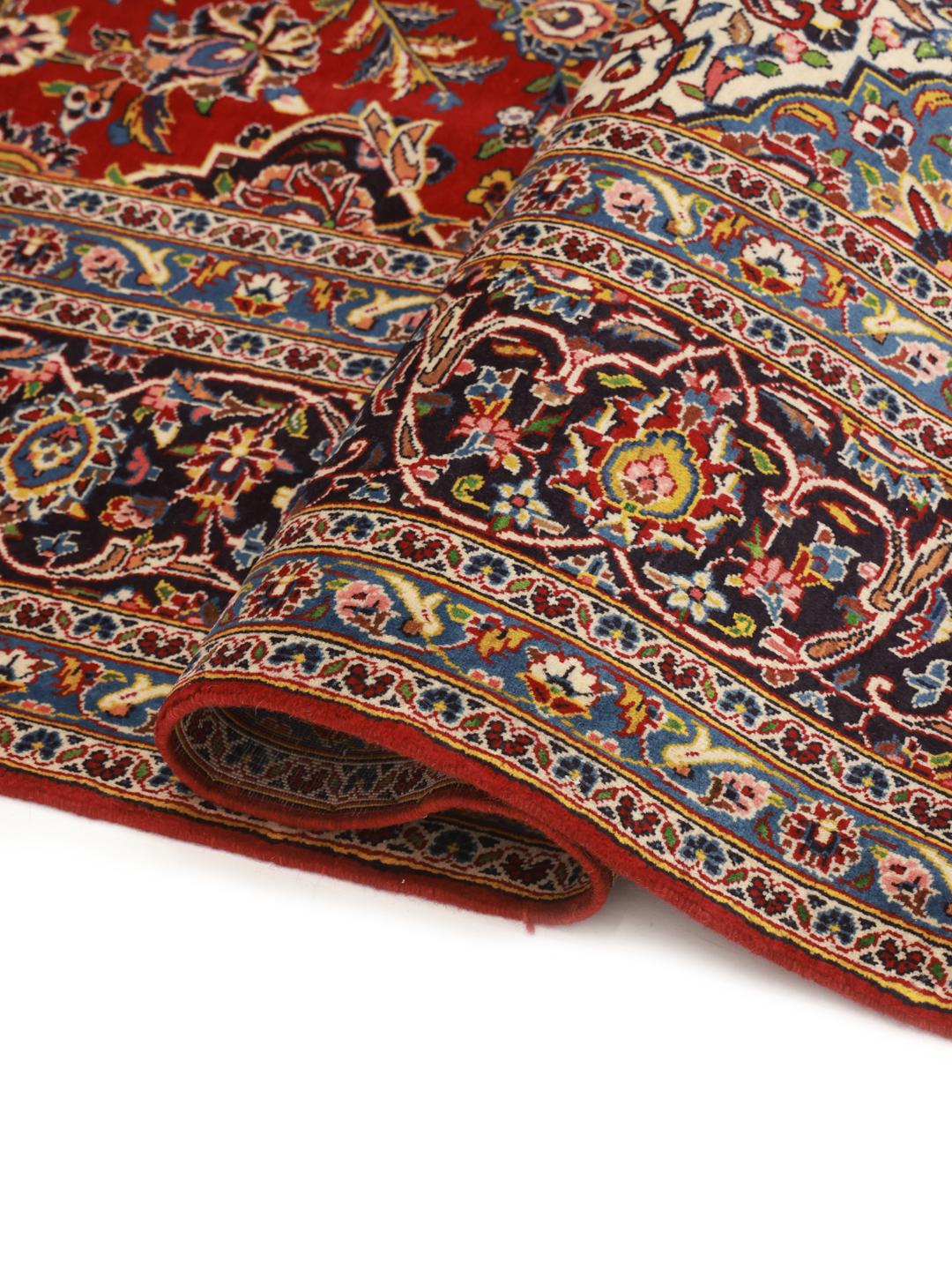 A large, hand-knotted Keshan rug from the Middle East with a deep red floral field and navy border.