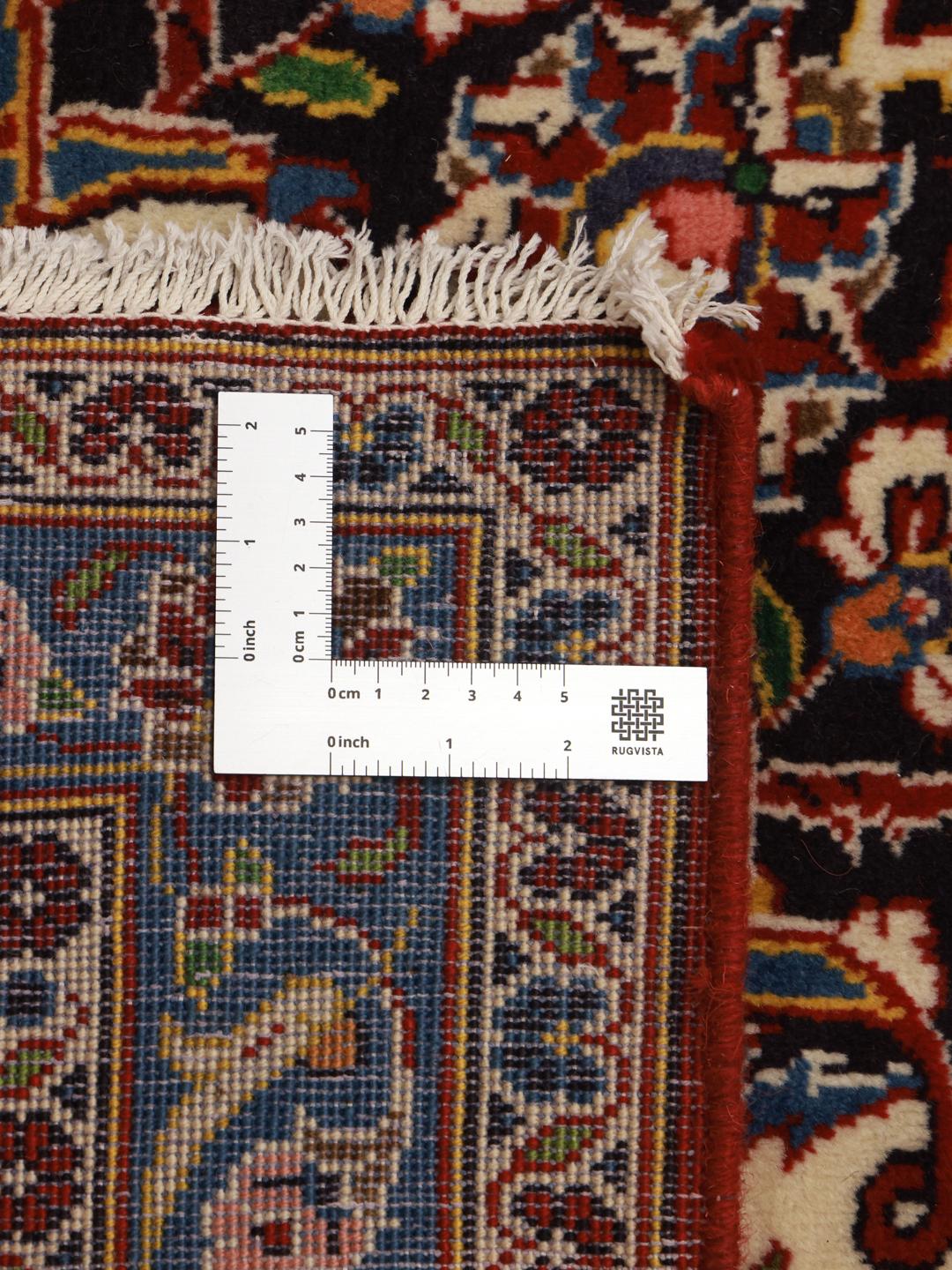 A large, hand-knotted Keshan rug from the Middle East with a deep red floral field and navy border.