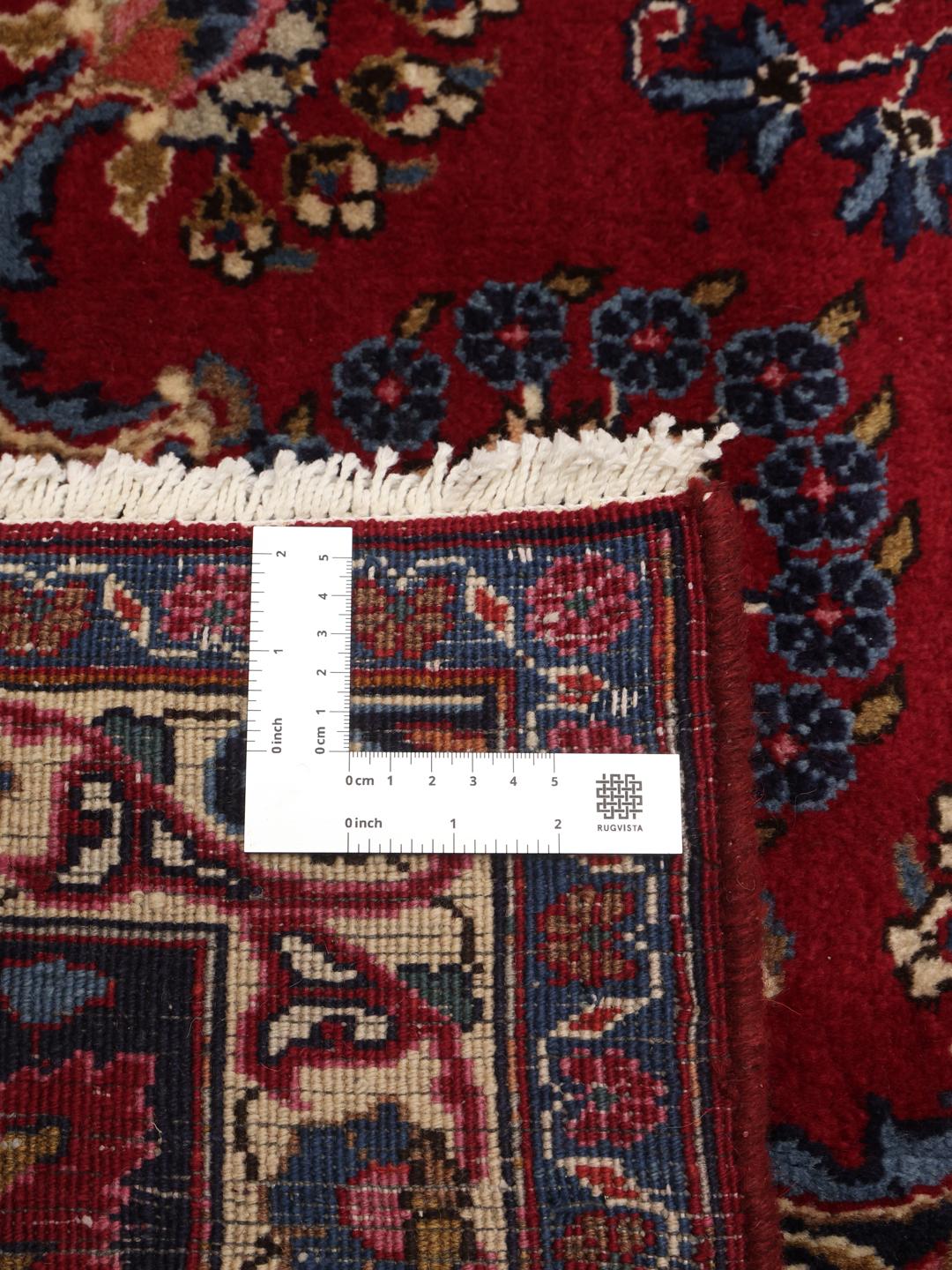 Et håndknyttet Mashad-tæppe fra Mellemøsten med en mørkerød bund og ornamenterede blomstermønstre.