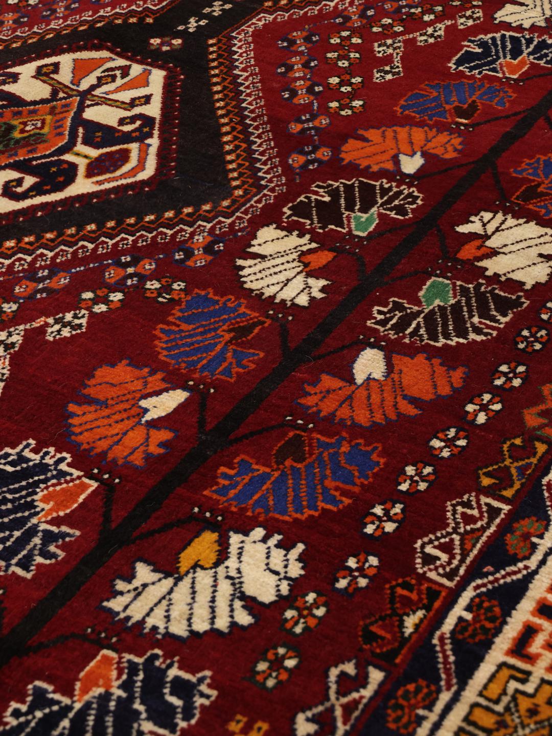 A hand-knotted Qashqai rug from the Middle East featuring a vibrant red field and geometric medallion patterns.