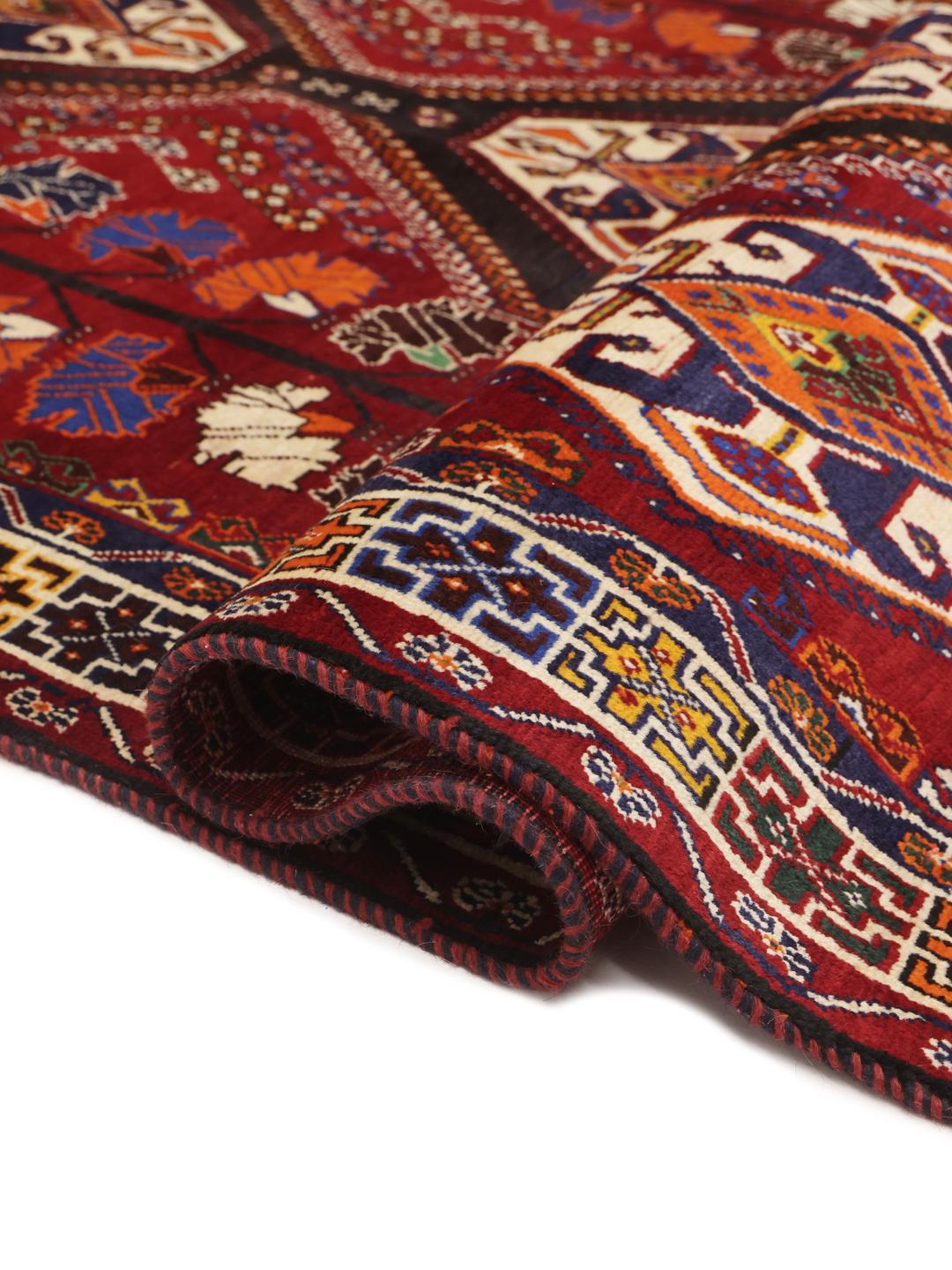 A hand-knotted Qashqai rug from the Middle East featuring a vibrant red field and geometric medallion patterns.
