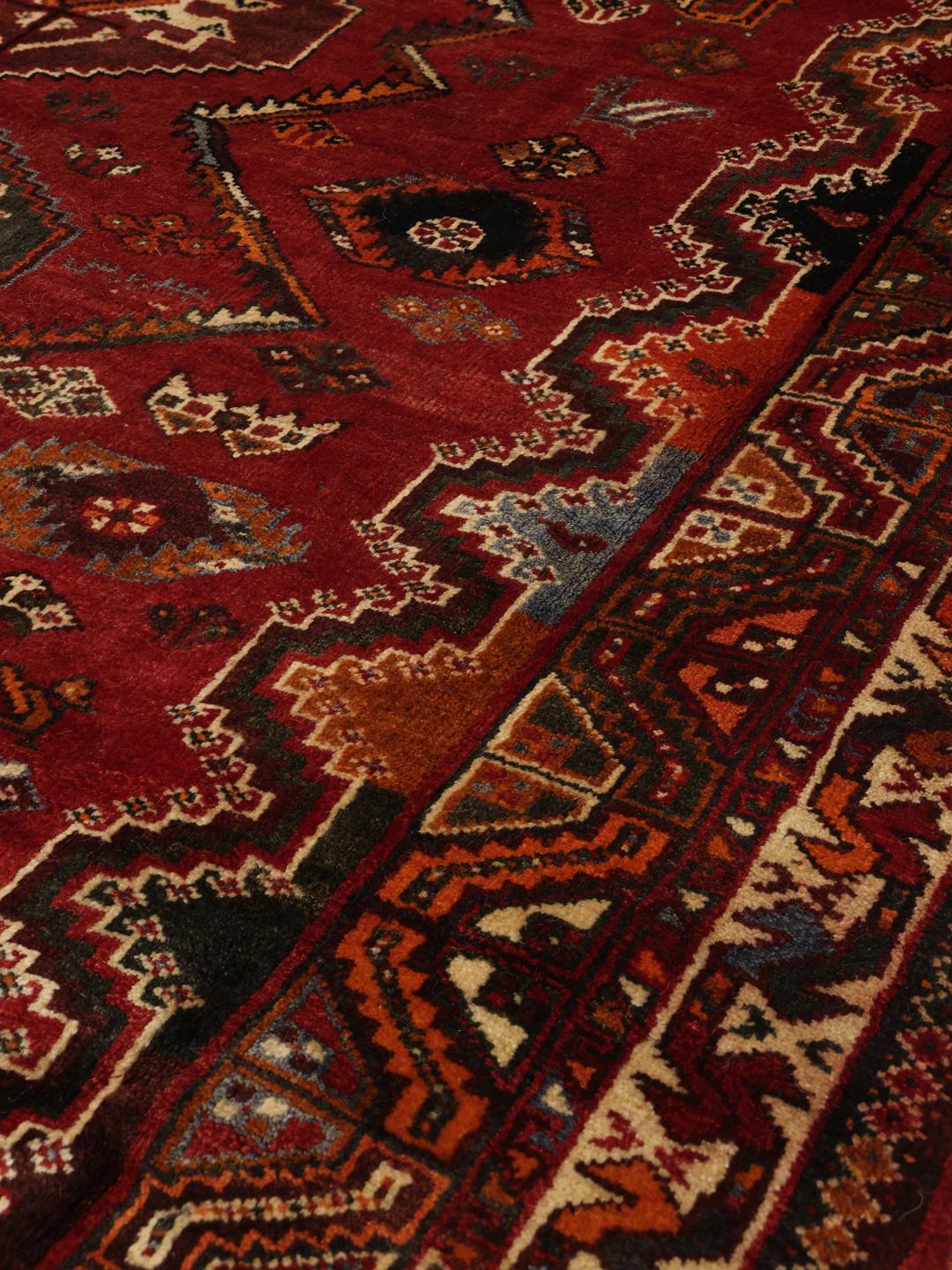 A hand-knotted Ghashghai rug from the Middle East featuring a vibrant red and dark-blue geometric design.
