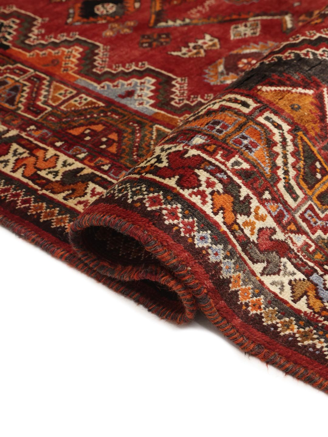 A hand-knotted Ghashghai rug from the Middle East featuring a vibrant red and dark-blue geometric design.