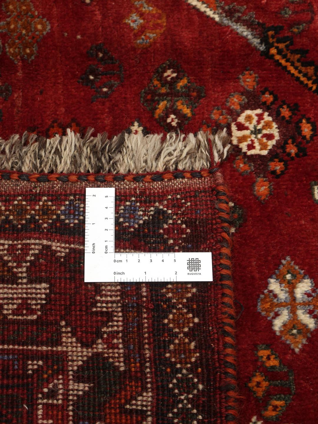 A hand-knotted Ghashghai rug from the Middle East featuring a vibrant red and dark-blue geometric design.