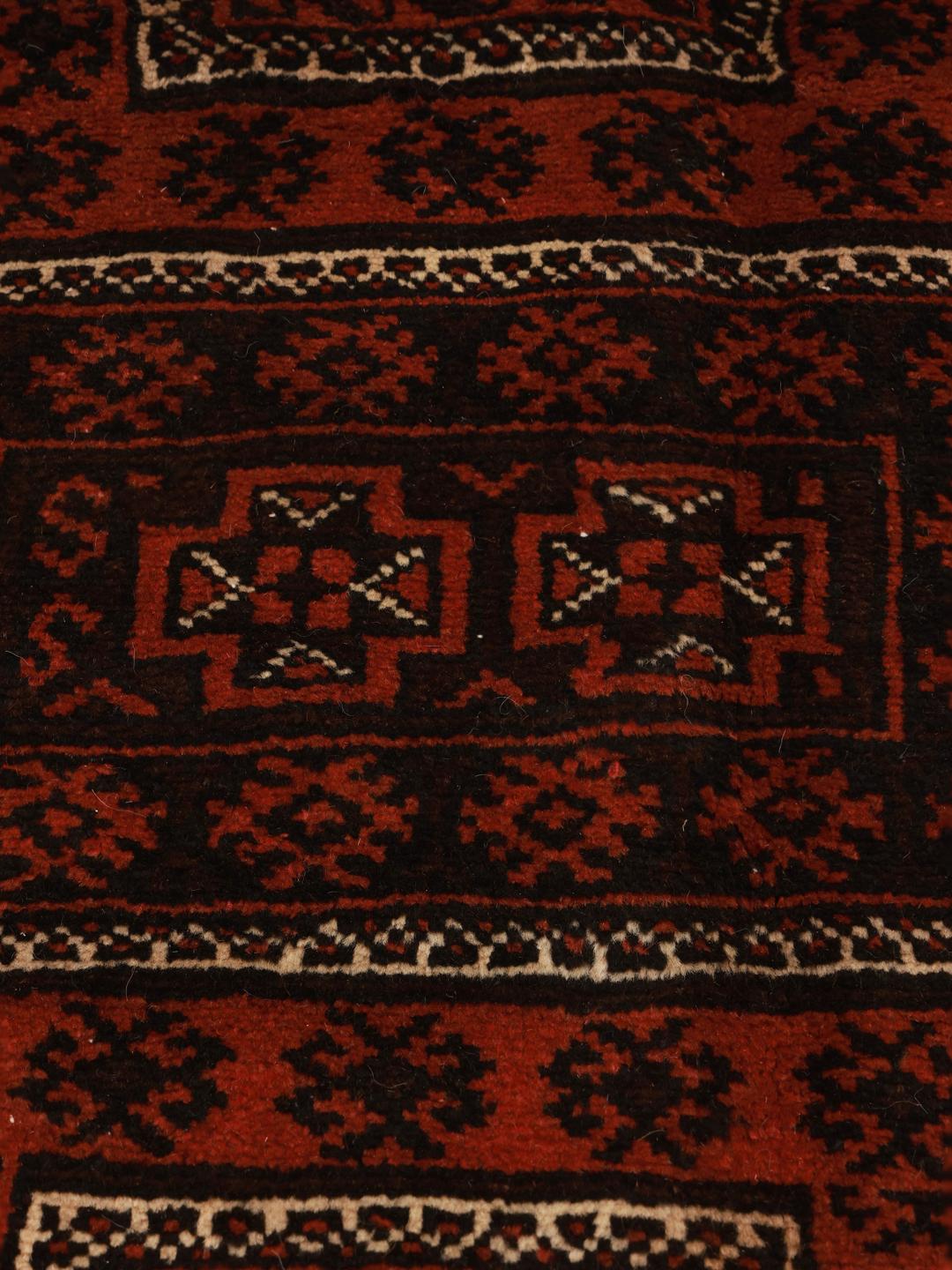 A hand-knotted Baluch rug with a dark-red field and geometric motifs from the Middle East.