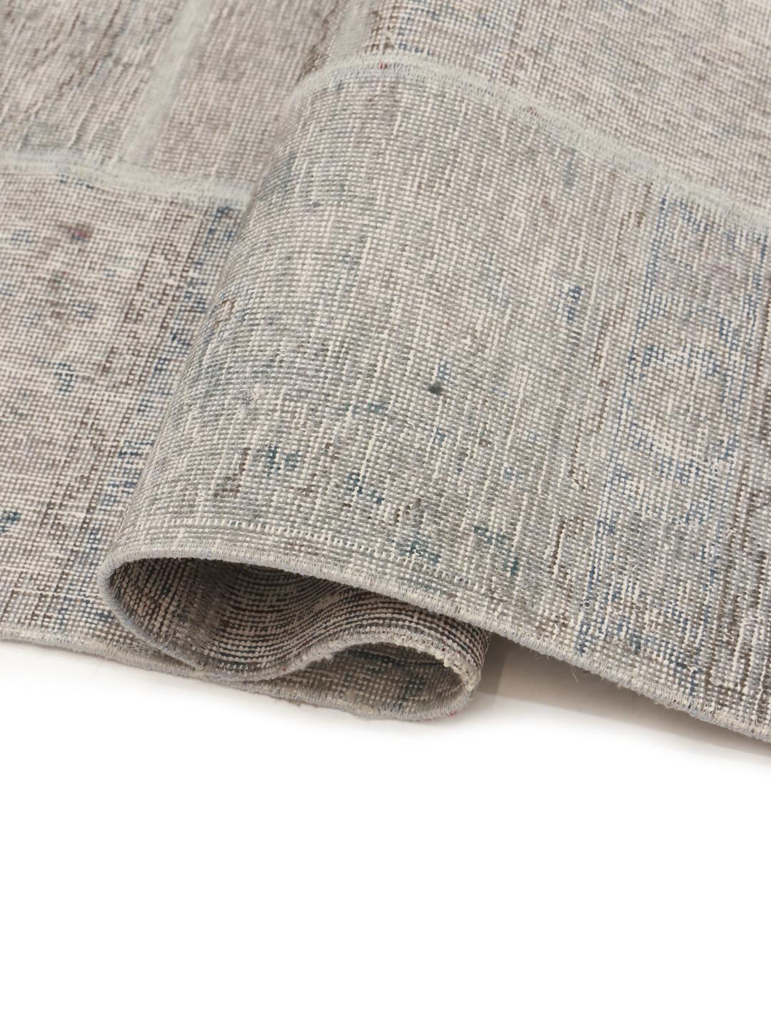 Et unikt patchwork-tæppe lavet af håndknyttede uldfragmenter i grå nuancer.