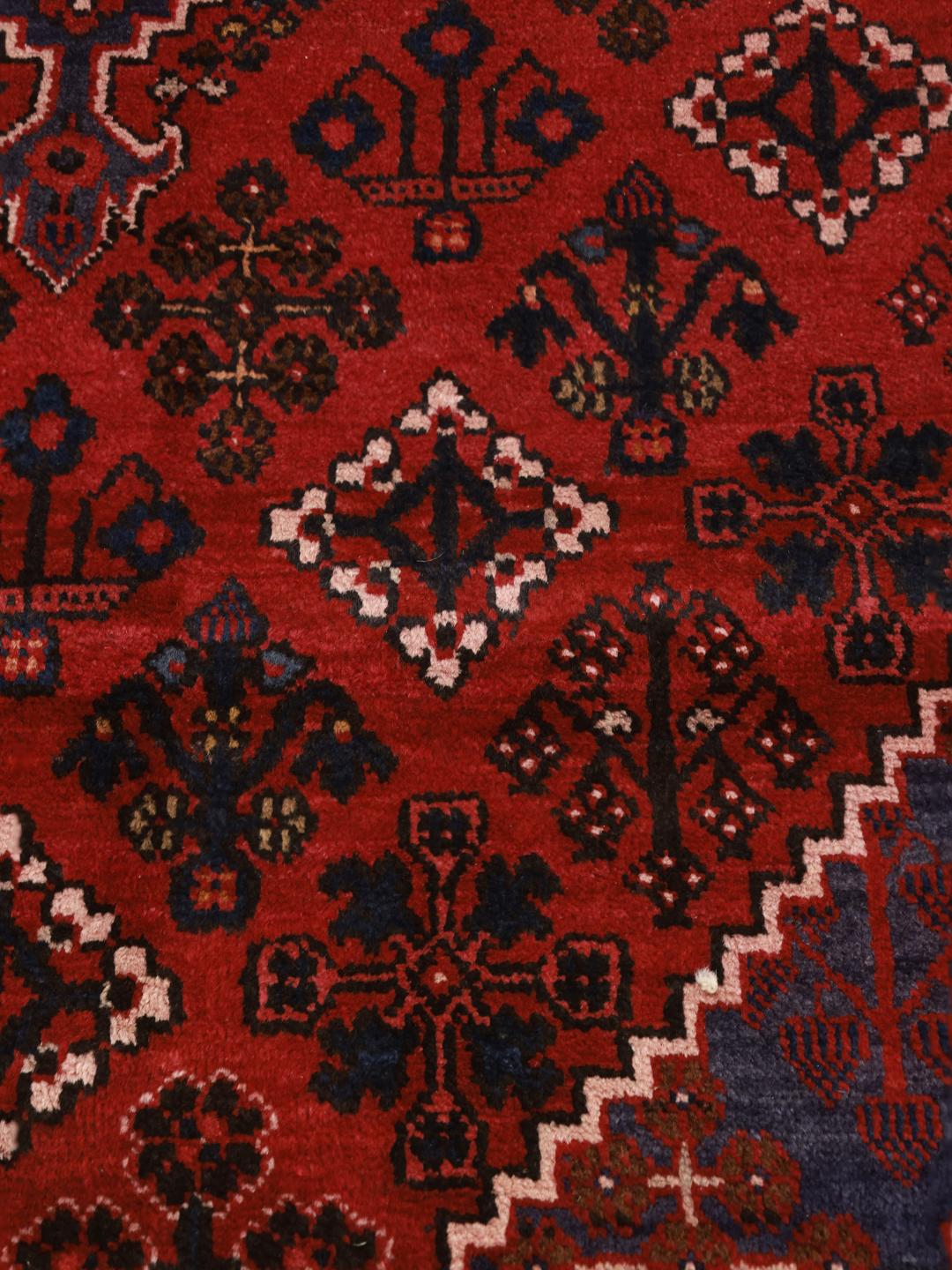 Een handgeknoopt Joshaghan-tapijt uit het Midden-Oosten met een rood veld en geometrische bloempatronen.