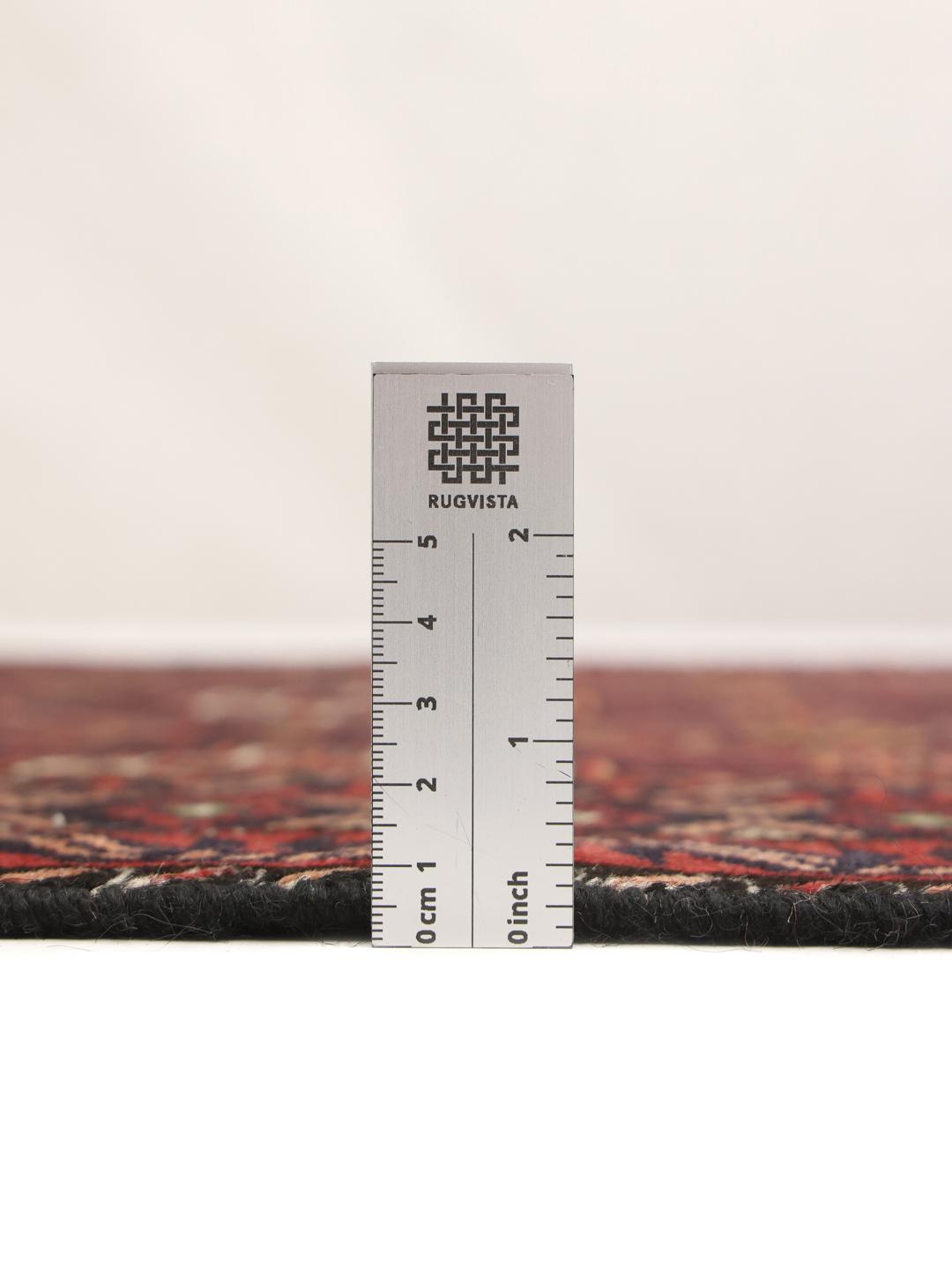 Et håndlavet Baluch-tæppe fra Mellemøsten med et mørkerødt og sort geometrisk mønster.