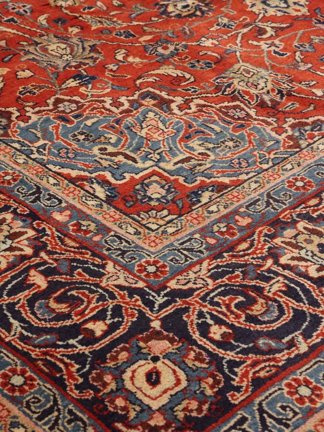 Een groot rechthoekig handgeknoopt Sarough-tapijt uit het Midden-Oosten met een rood en blauw bloemenpatroon.