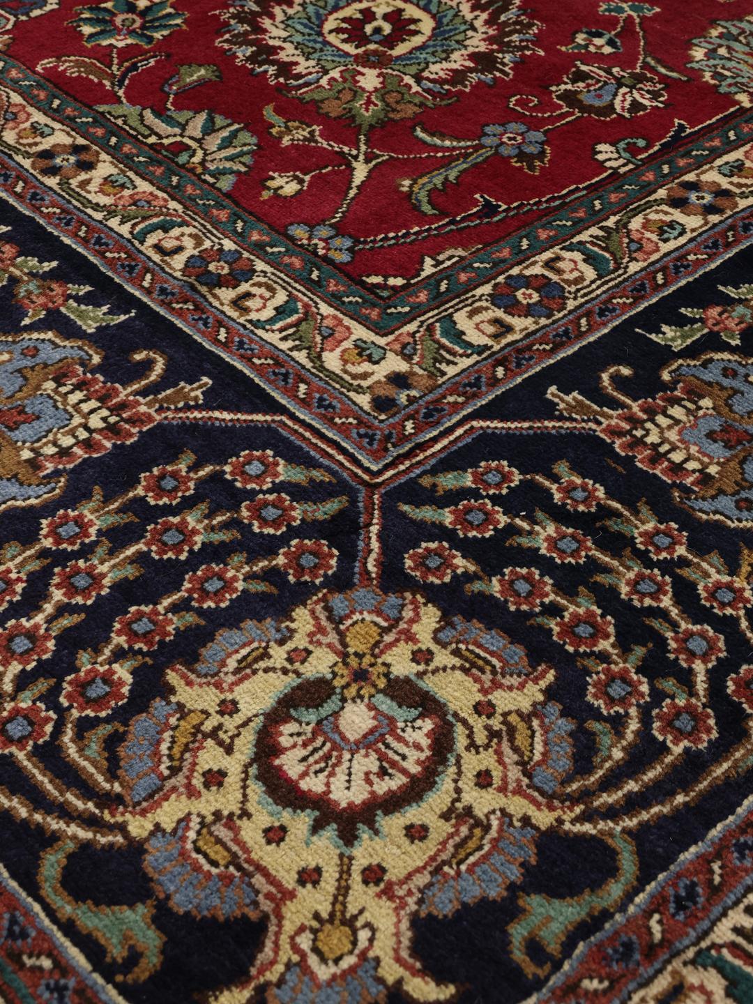 Een groot rechthoekig Tabriz-tapijt uit het Midden-Oosten met een rood veld en een blauwe rand.