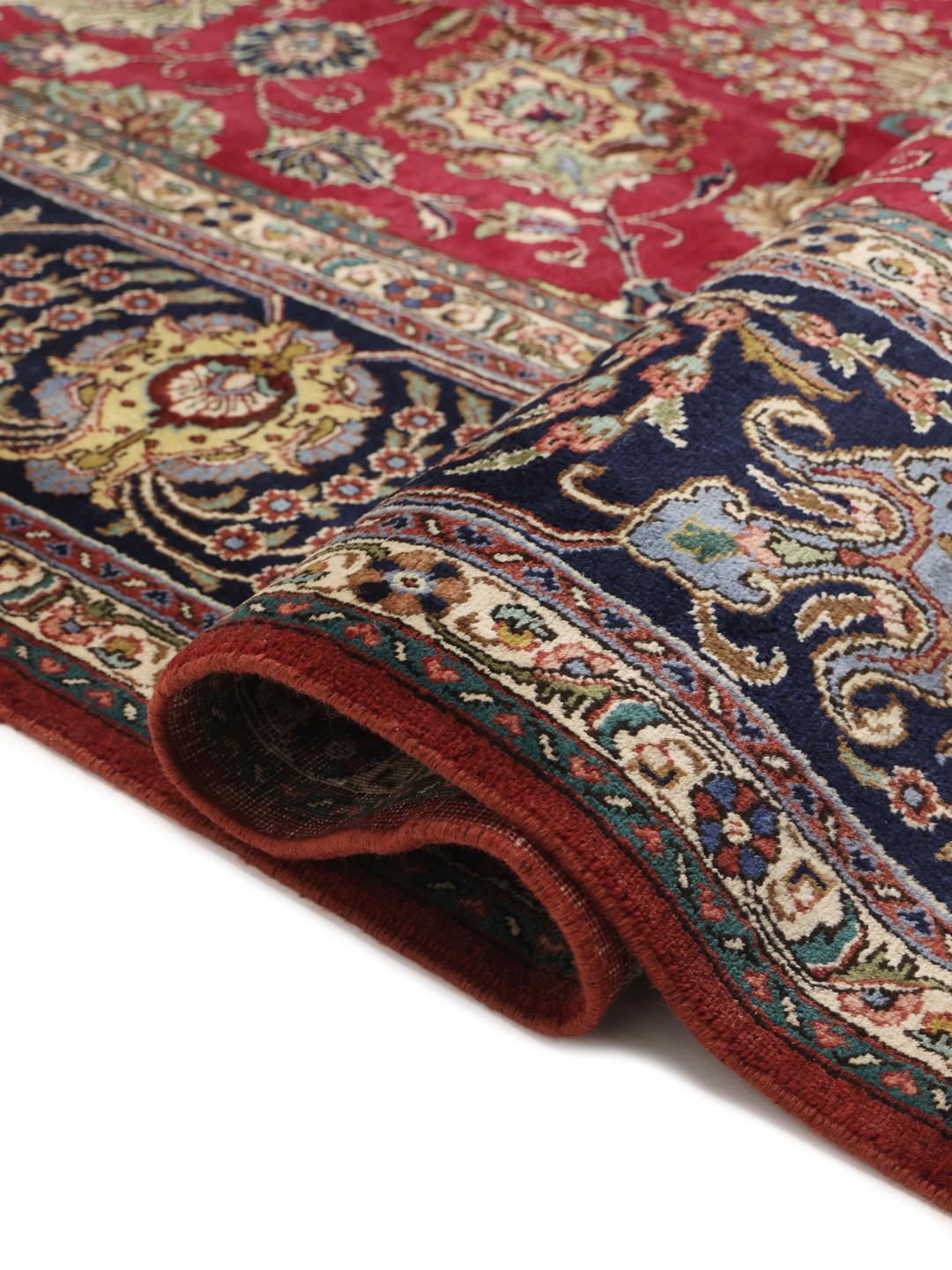 Een groot rechthoekig Tabriz-tapijt uit het Midden-Oosten met een rood veld en een blauwe rand.