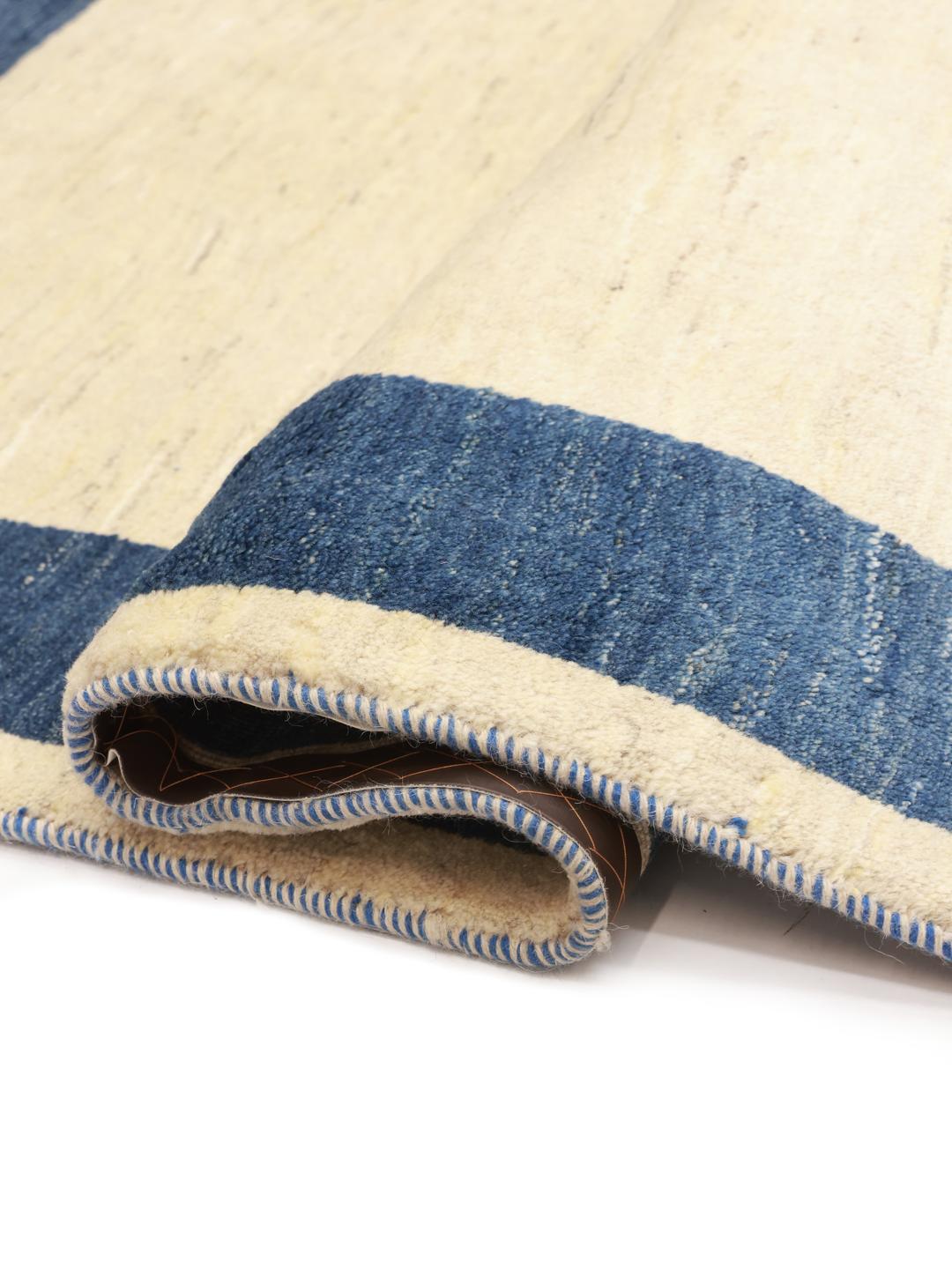 Tapis Gabbeh noué à la main venant du Moyen-Orient avec un champ beige et une bordure bleu foncé.