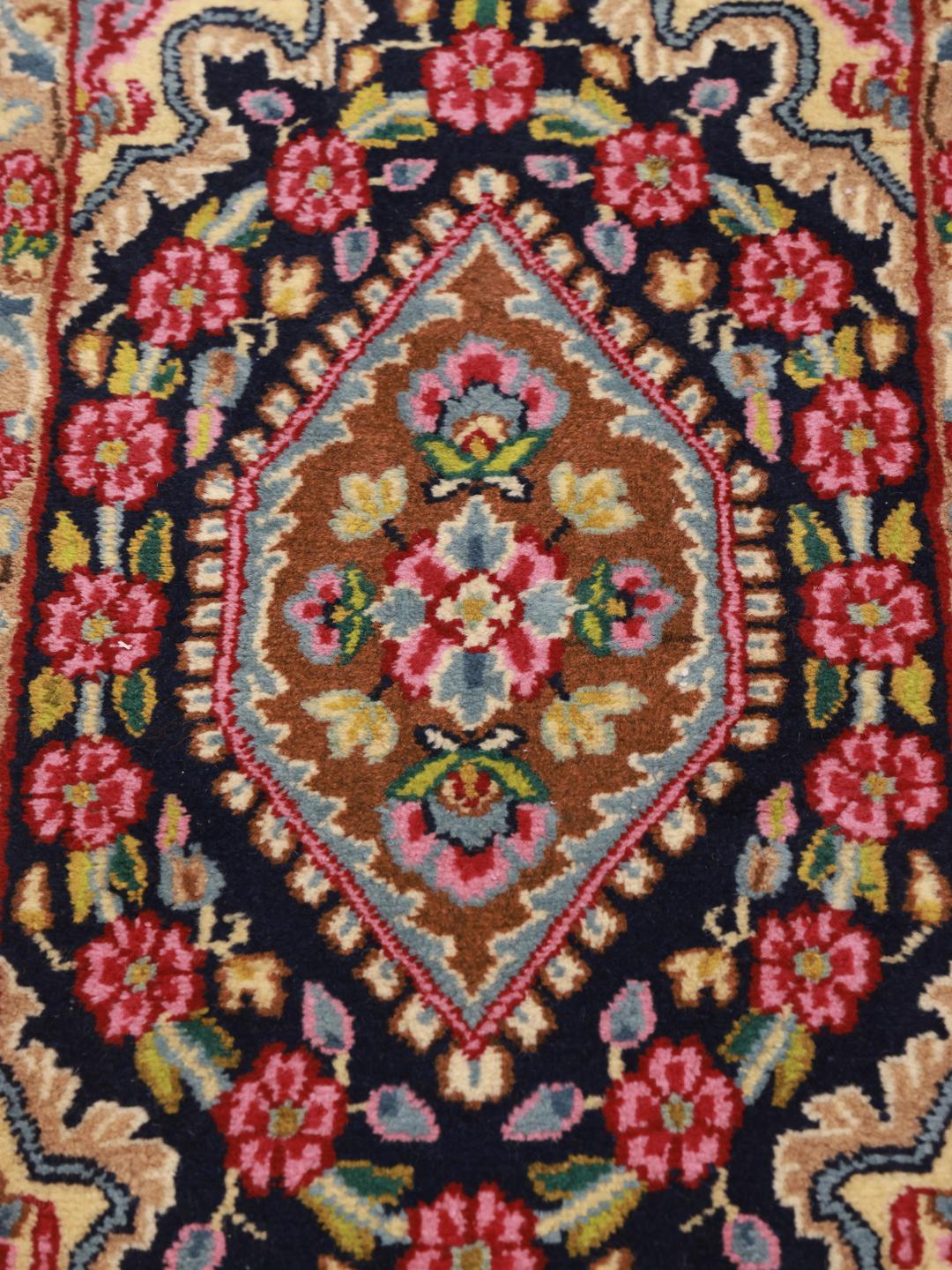 A hand-knotted Kerman rug from the Middle East with a red field and floral patterns.