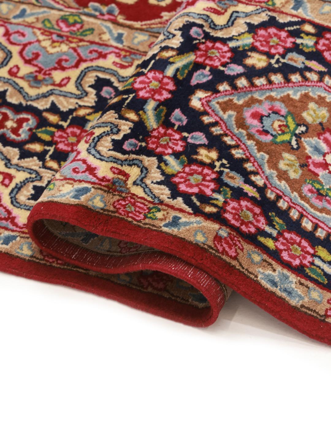 A hand-knotted Kerman rug from the Middle East with a red field and floral patterns.