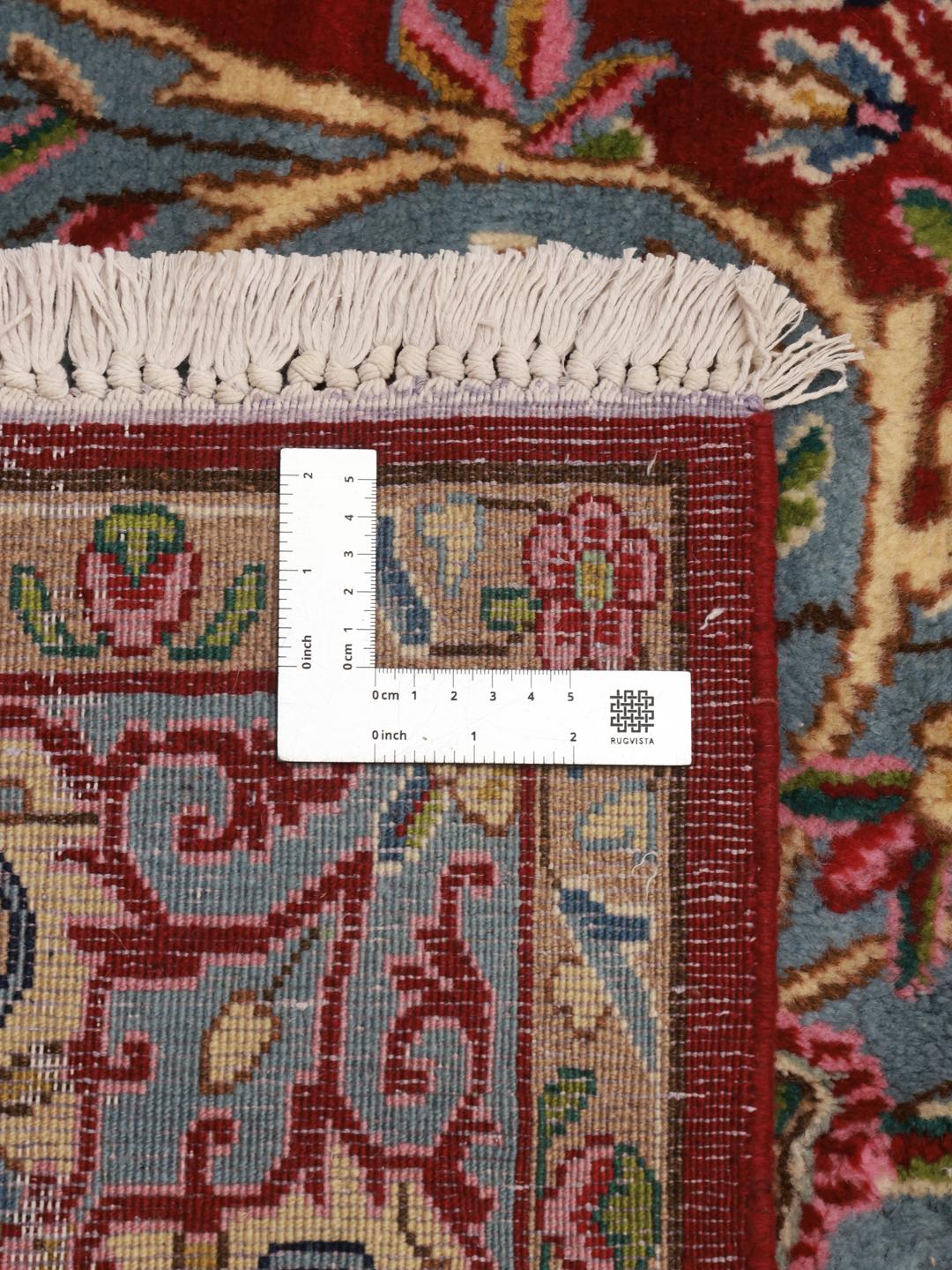 A hand-knotted Kerman rug from the Middle East with a red field and floral patterns.