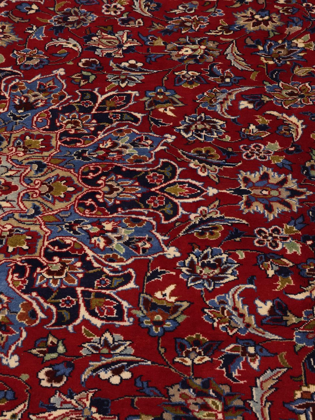 Een groot rechthoekig handgeknoopt Najafabad-tapijt met een rood veld en blauwe bloempatronen uit het Midden-Oosten.