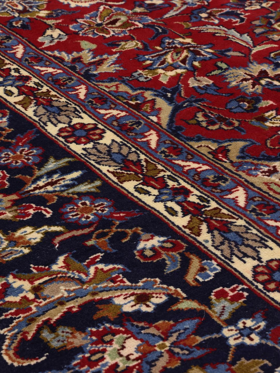Een groot rechthoekig handgeknoopt Najafabad-tapijt met een rood veld en blauwe bloempatronen uit het Midden-Oosten.