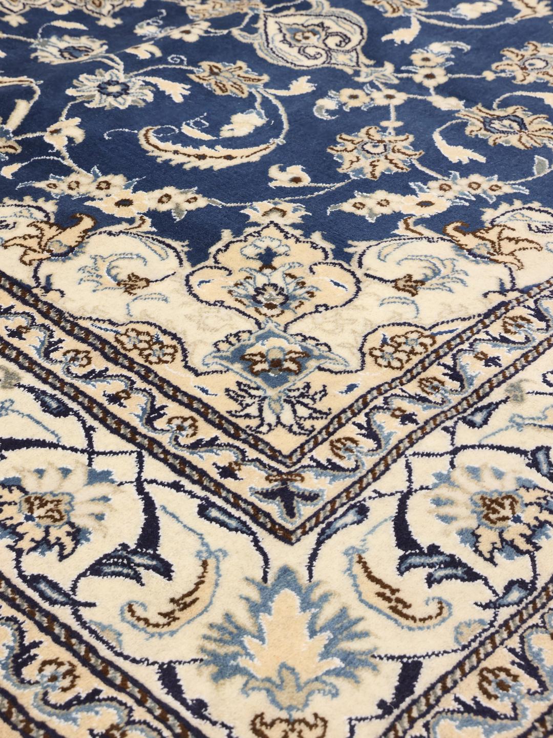 A hand-knotted Nain rug from the Middle East with a deep blue and cream floral pattern.