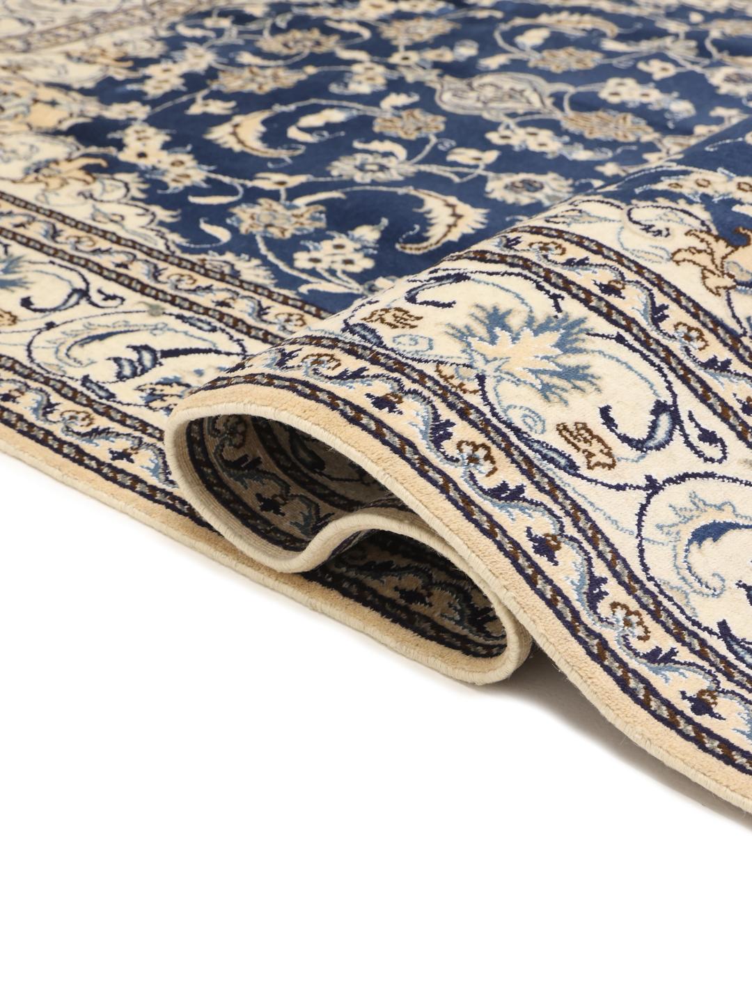 A hand-knotted Nain rug from the Middle East with a deep blue and cream floral pattern.