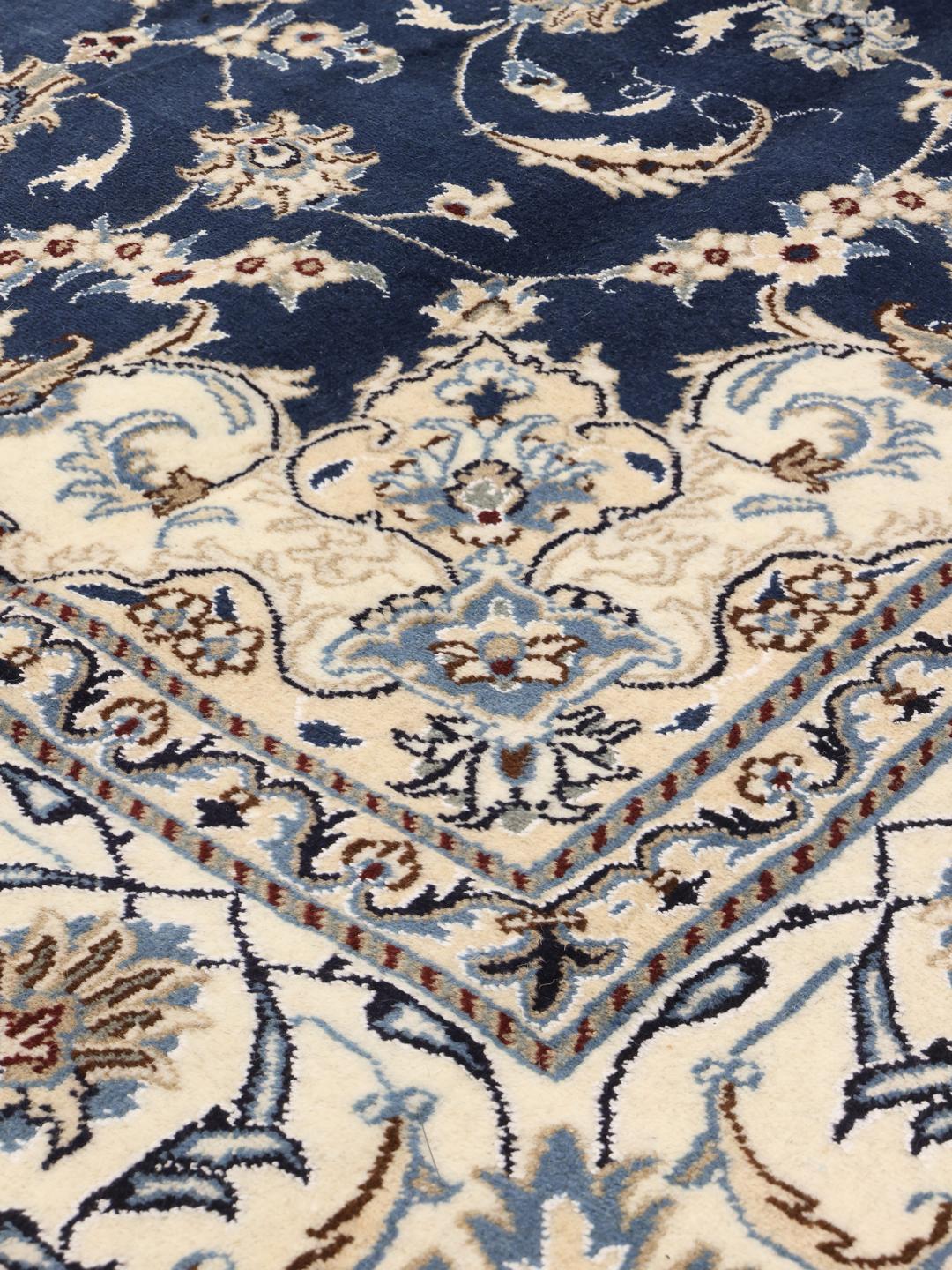 A hand-knotted Nain rug from the Middle East featuring a blue field with floral patterns.