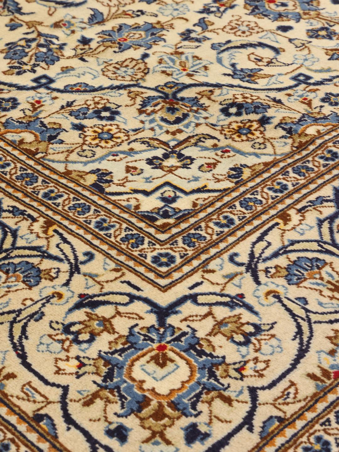 Een handgeknoopt Keshan tapijt uit het Midden-Oosten met een beige veld en blauwe bloemenmedaillonpatronen.