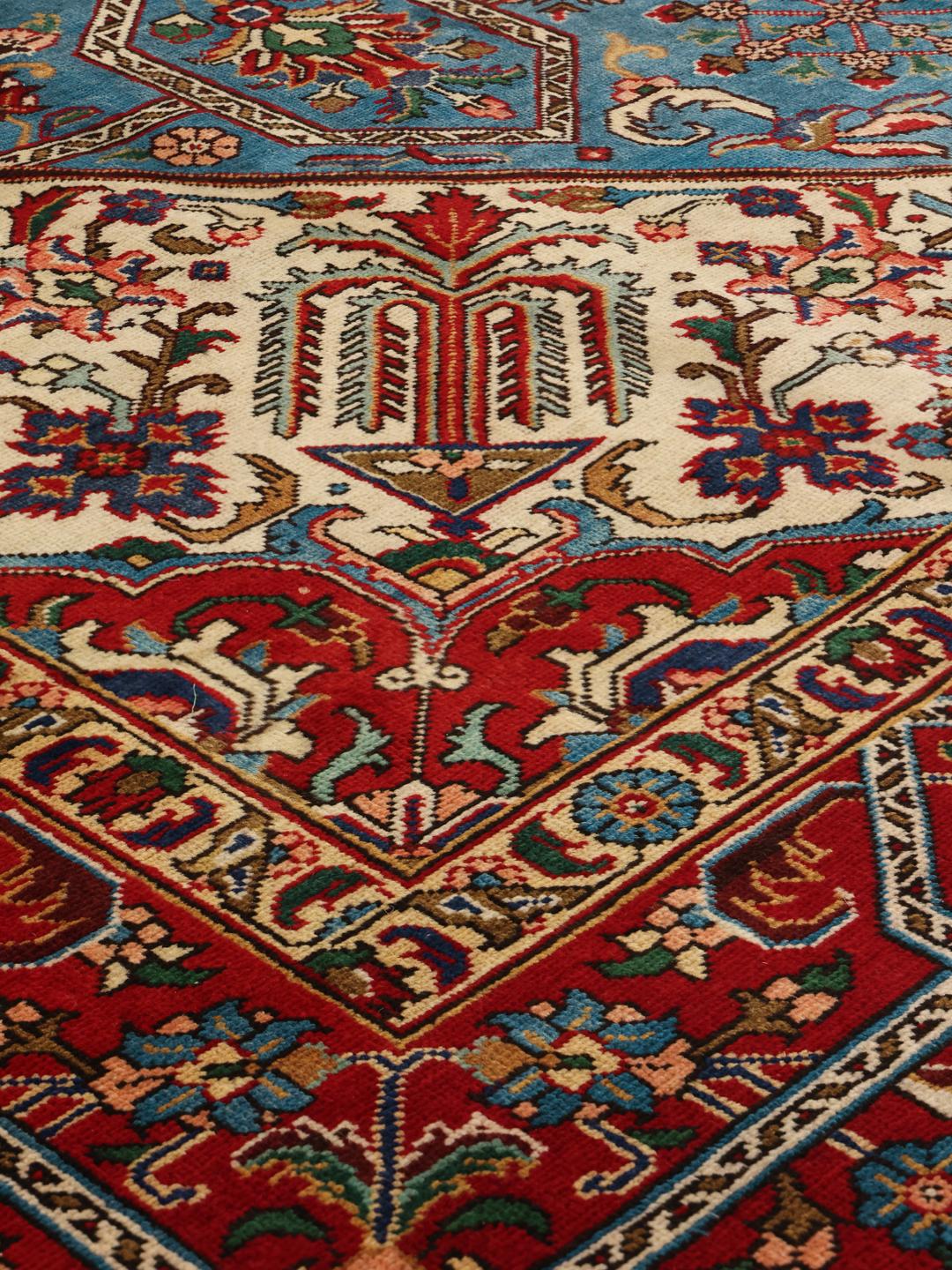 Een groot rechthoekig Tabriz-tapijt uit het Midden-Oosten met een levendig rood en blauwgroen kleurenpalet en sierlijke bloemmotieven.