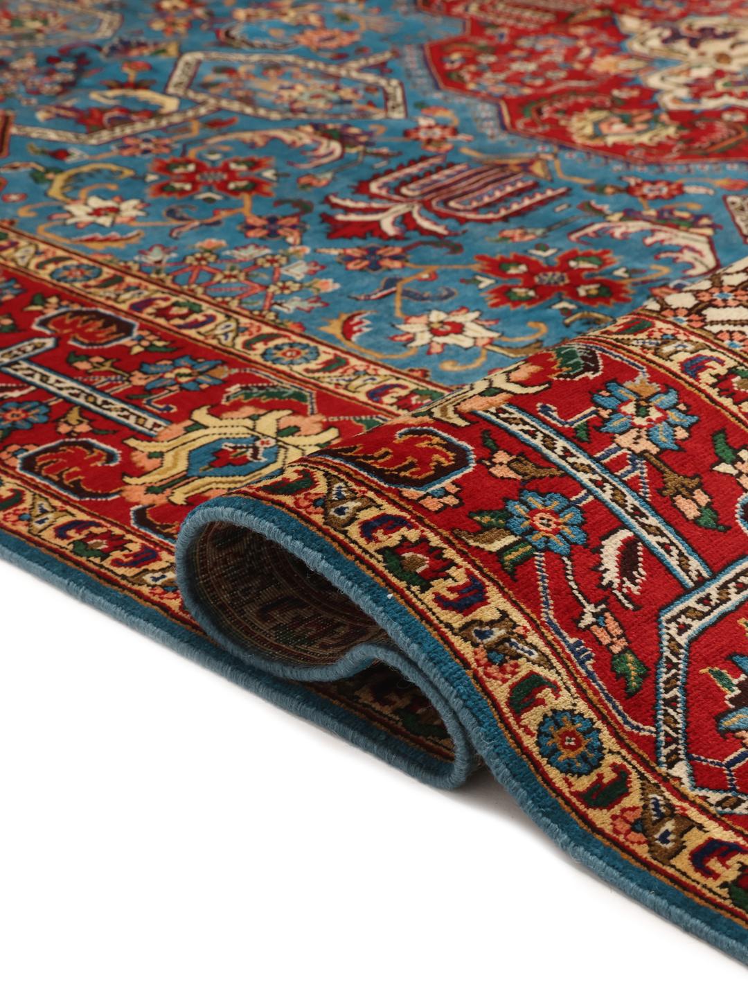 Een groot rechthoekig Tabriz-tapijt uit het Midden-Oosten met een levendig rood en blauwgroen kleurenpalet en sierlijke bloemmotieven.