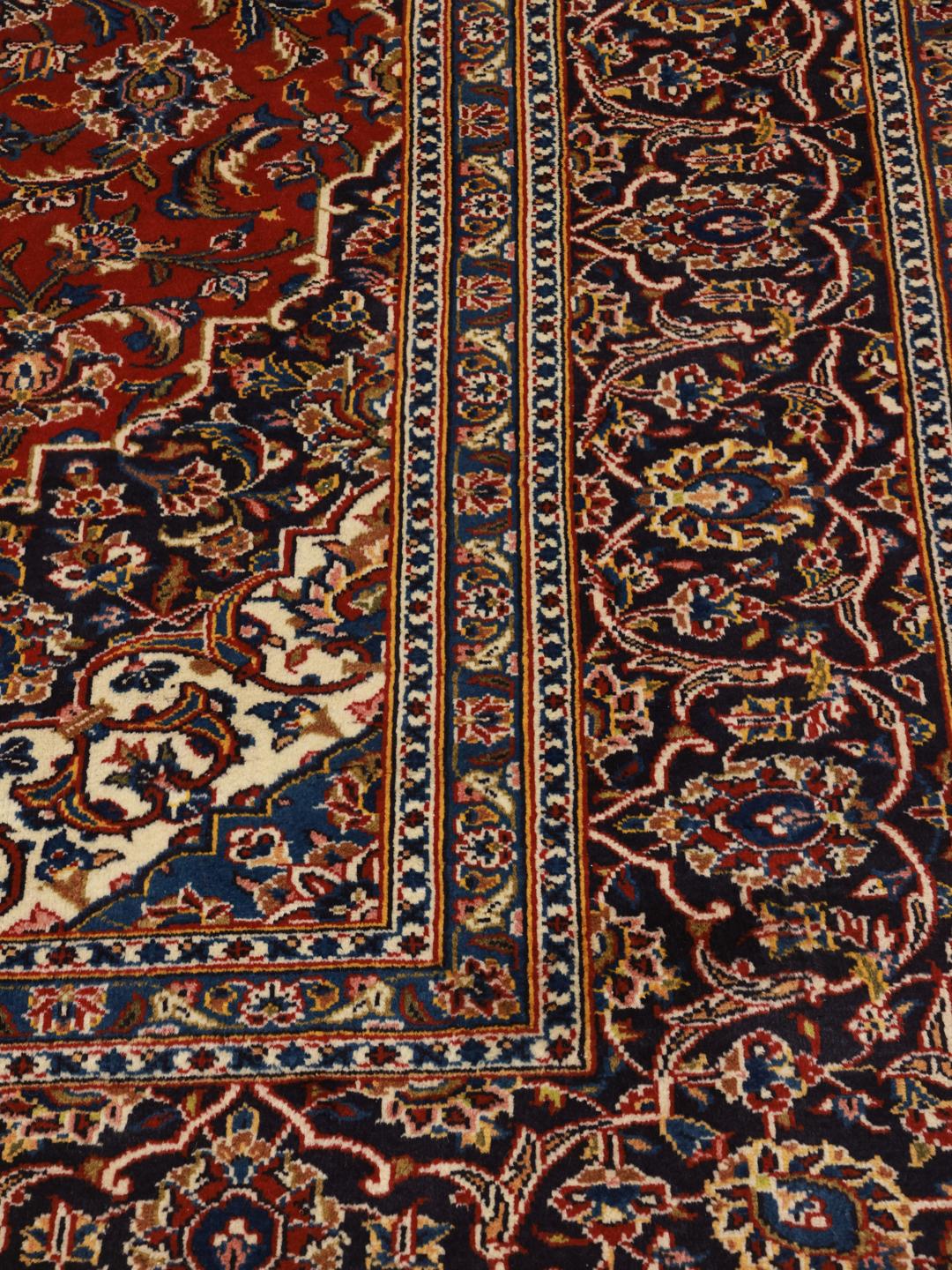 Een met de hand geknoopt Keshan-tapijt uit het Midden-Oosten met een levendig rood en donkerblauw bloemenmedaillonontwerp.