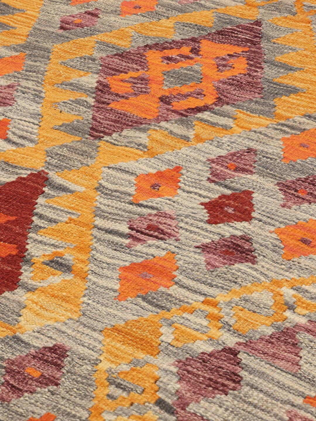 A large rectangular hand-woven Afghan Kelim rug featuring a vibrant geometric pattern in orange, red, and grey tones.