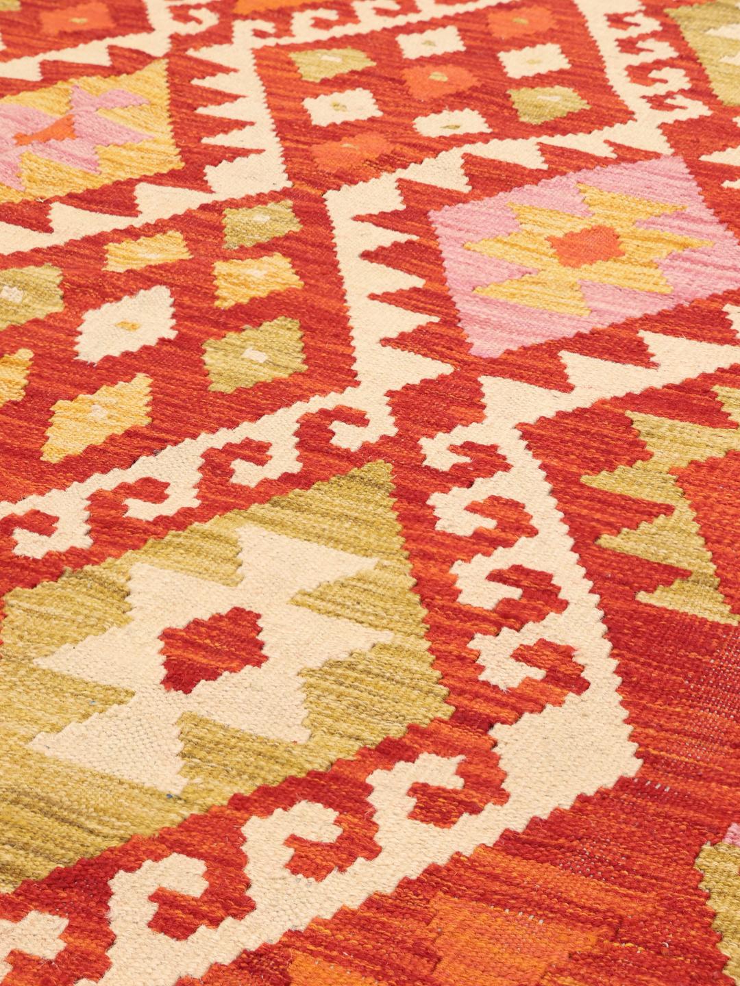 Hand-woven Afghan Kelim rug with geometric patterns in red, orange, and pink tones.