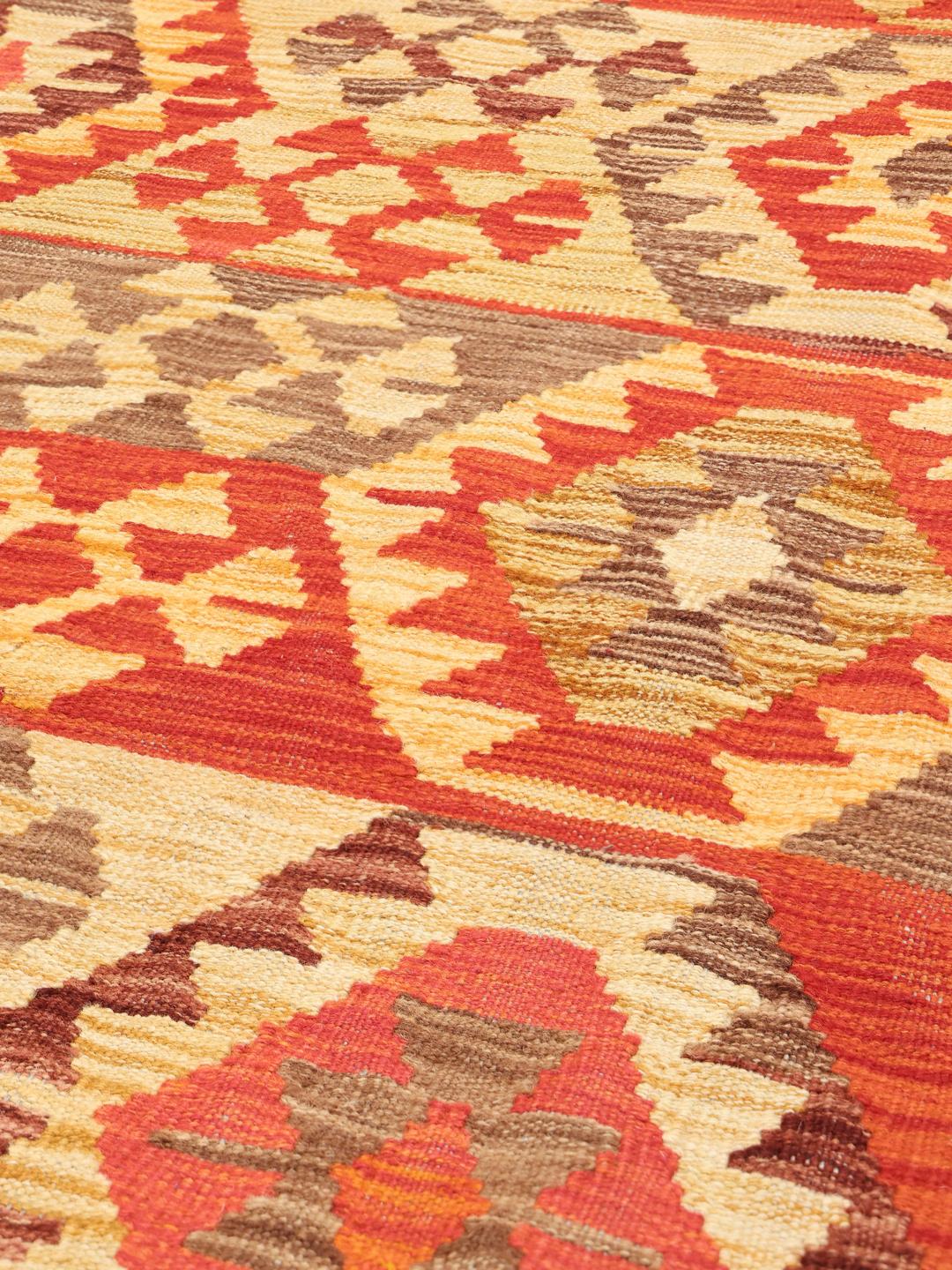 A hand-woven Afghan Kelim rug featuring geometric patterns in red, orange, and beige.
