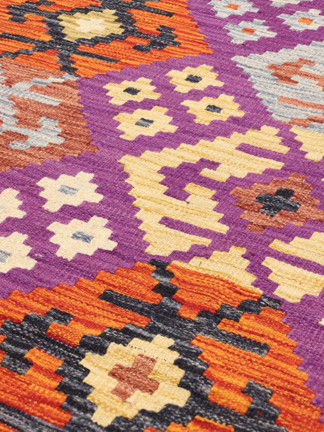 Et håndvævet Kelim-tæppe fra Afghanistan med en lilla bund og geometriske motiver.